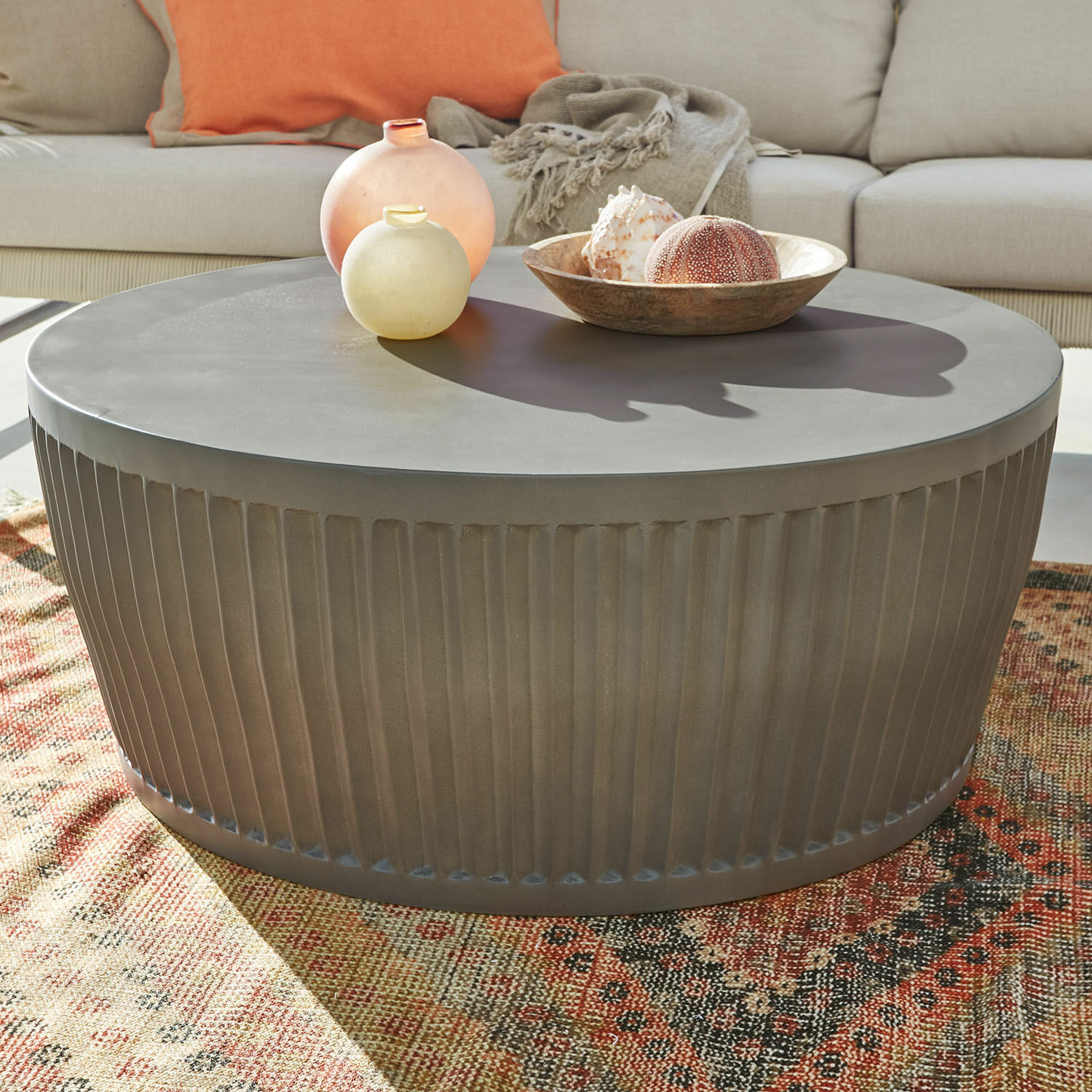 Table basse Vesalune Table basse ronde en métal gris avec base cannelée sur tapis coloré dans un salon lumineux