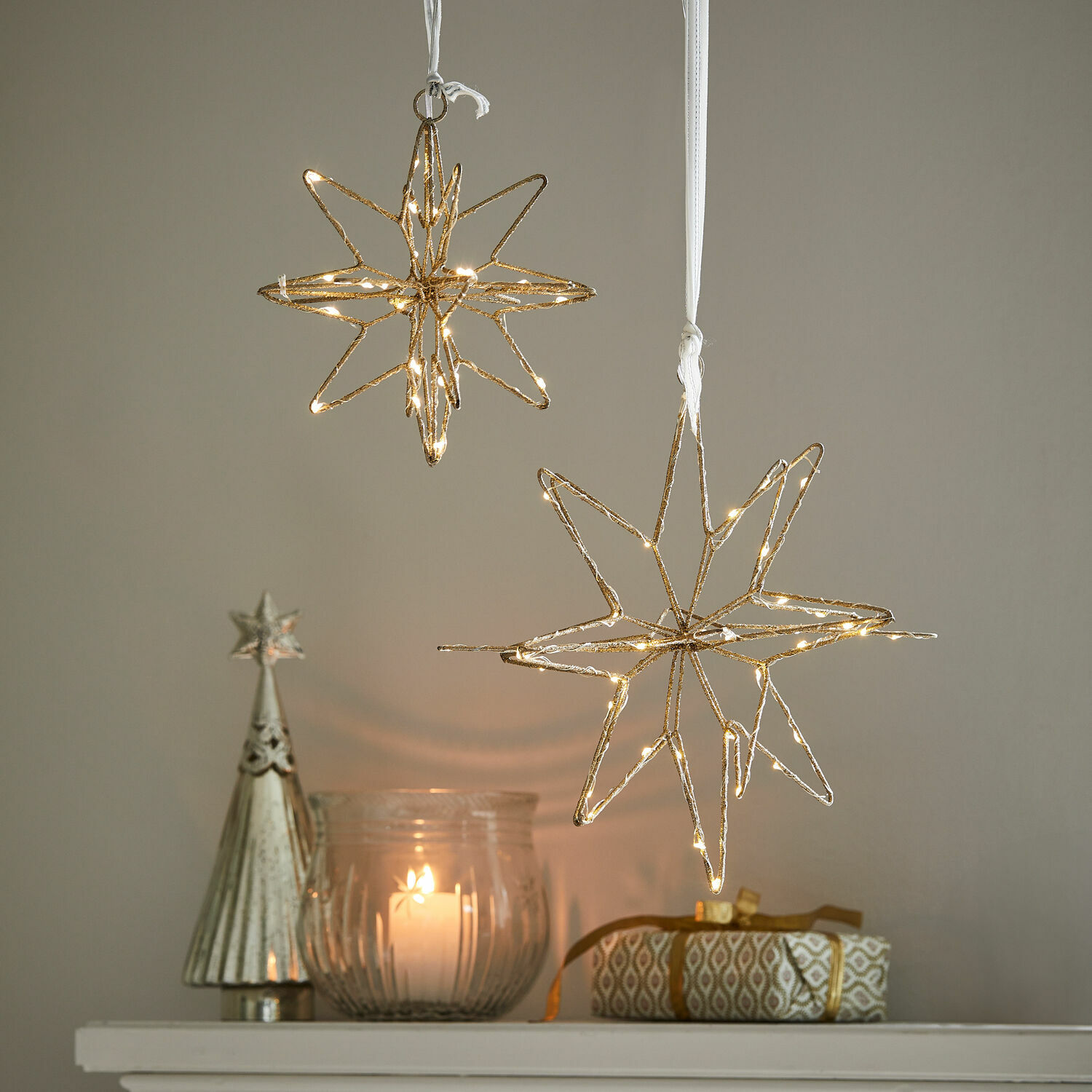 Ledster set van 2 Pérole Gouden LED-sterdecoraties hangend boven kaars en cadeau op witte plank