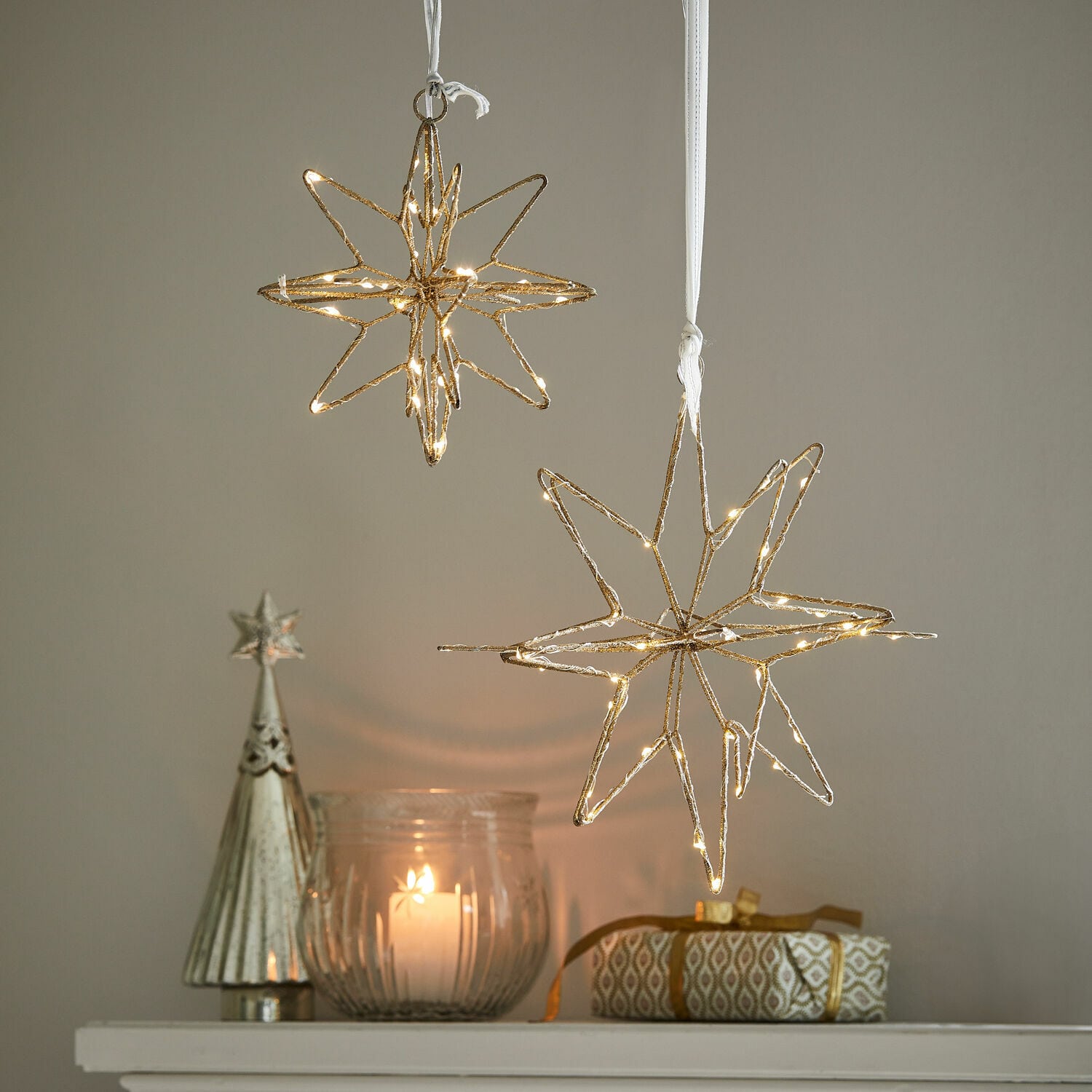 Ledster set van 2 Pérole Gouden LED-sterdecoraties hangend boven kaars en cadeau op witte plank