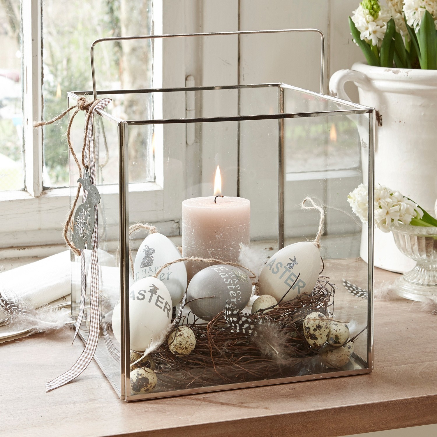 Glazen lantaarn met metalen frame, versierd met paaseieren en kaars op houten tafel
