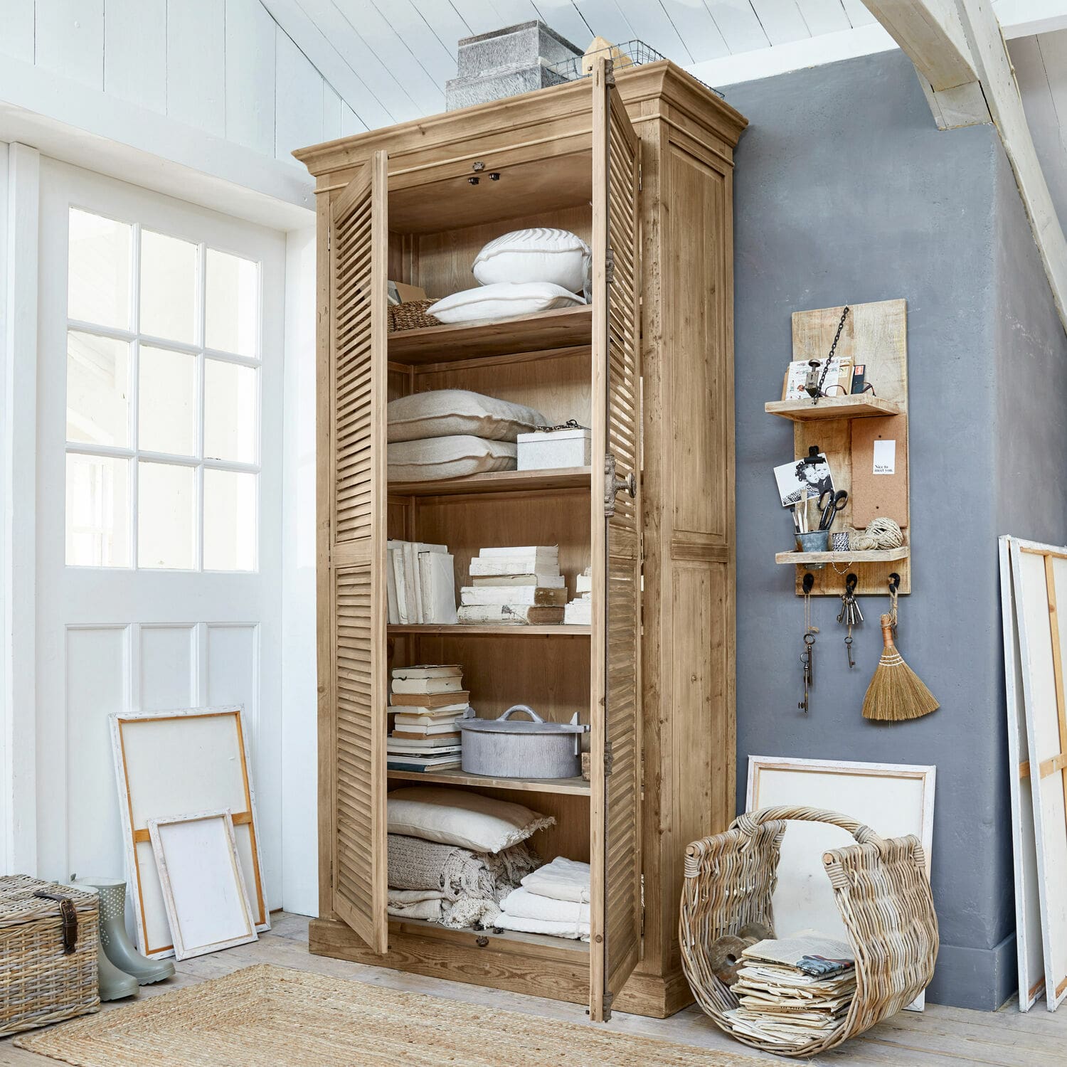 Kast Farnham Houten kast met luikdeuren in natuurlijke kleur, gevuld met kussens en boeken in lichte kamer
