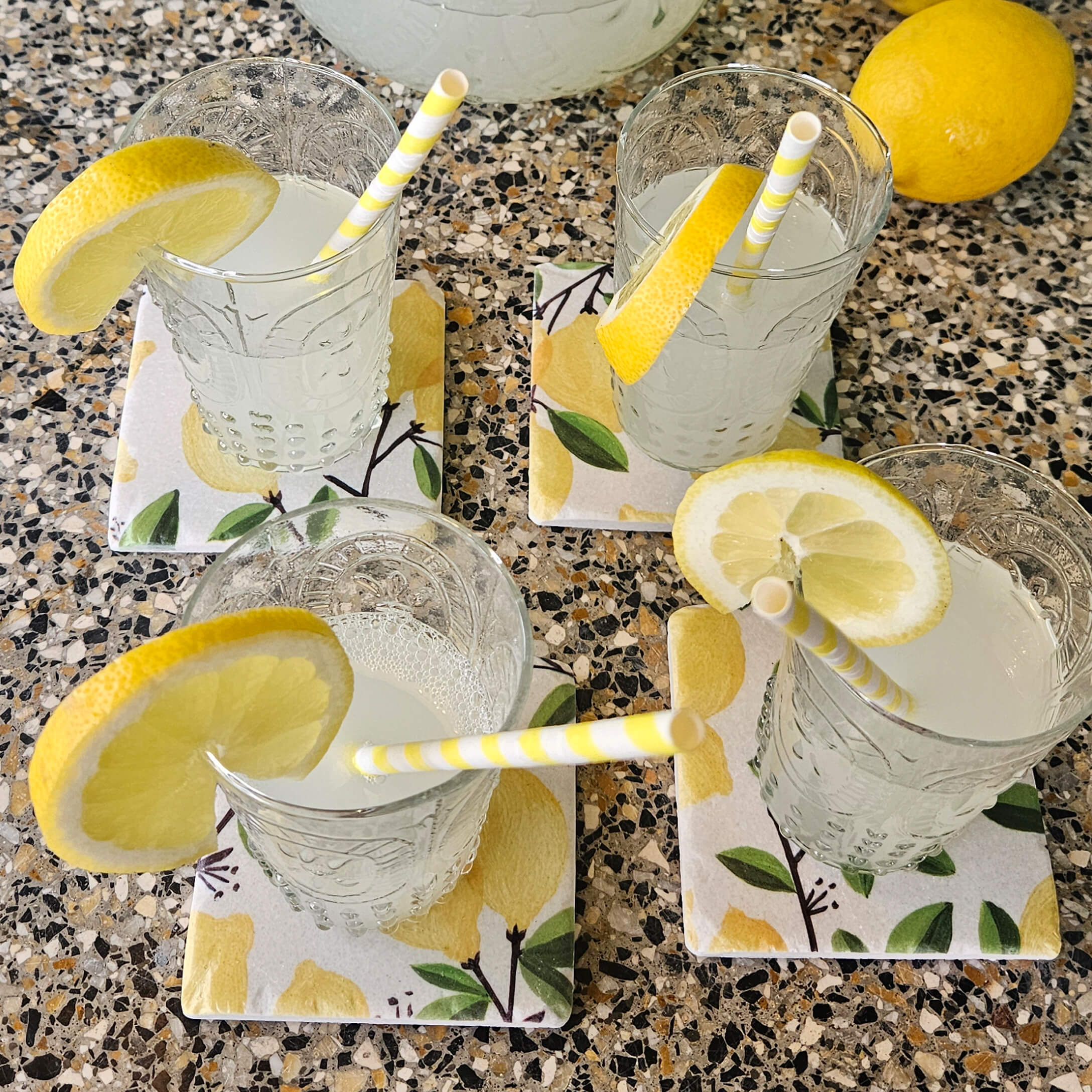 Verres de limonade avec tranches de citron sur des dessous de verre en céramique à motif citron sur un comptoir en pierre