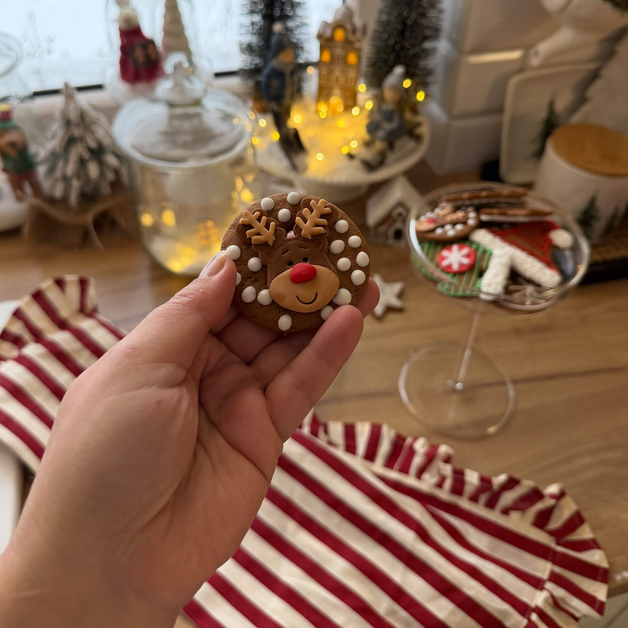 Main tenant un biscuit au pain d'épices décoré d'un renne avec des points blancs, décorations de Noël en arrière-plan
