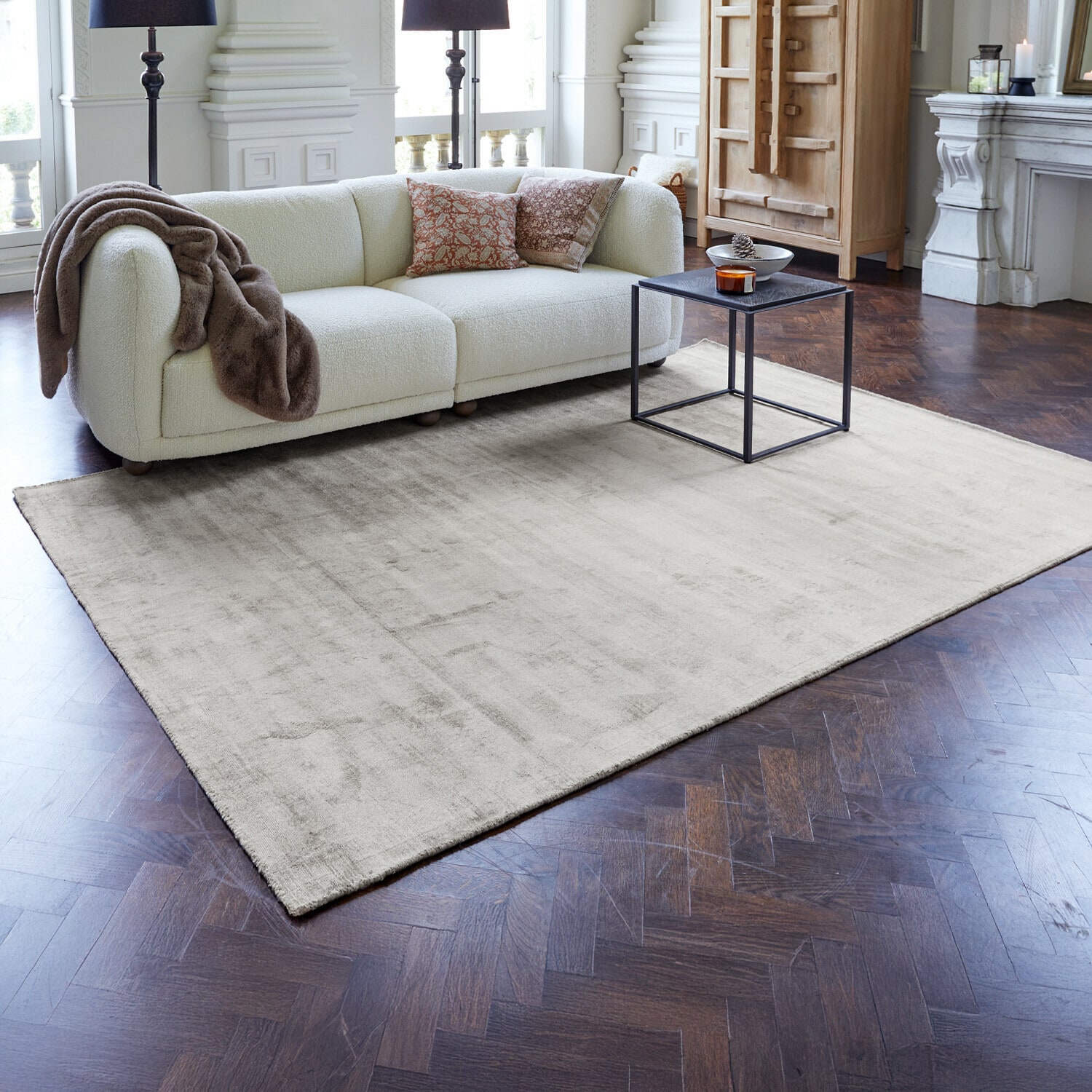 Vloerkleed Mariselle Lichtbeige vloerkleed op donkere houten vloer in moderne woonkamer met witte bank en zwarte tafel
