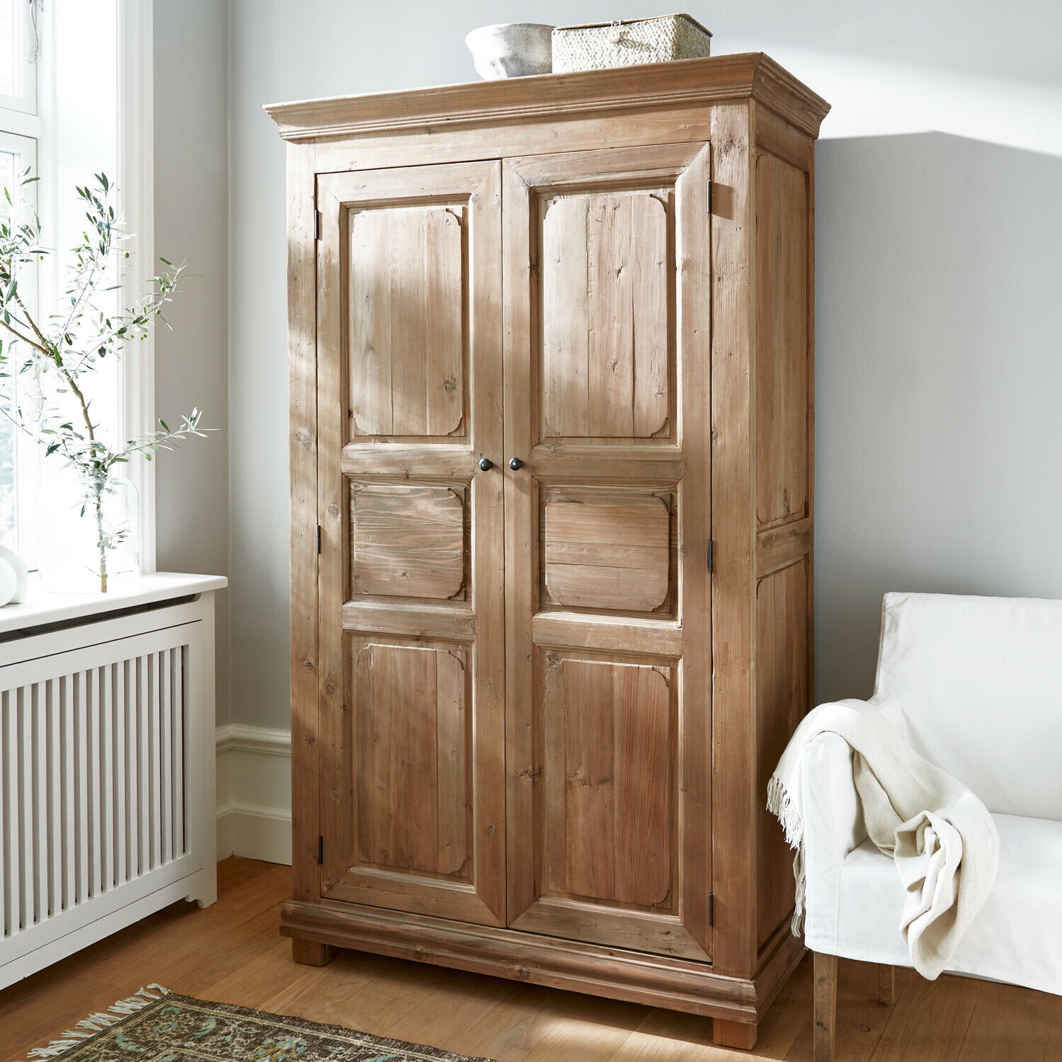 Armoire Gavrielle Armoire en bois naturel dans une pièce lumineuse avec fauteuil blanc et tapis décoratif