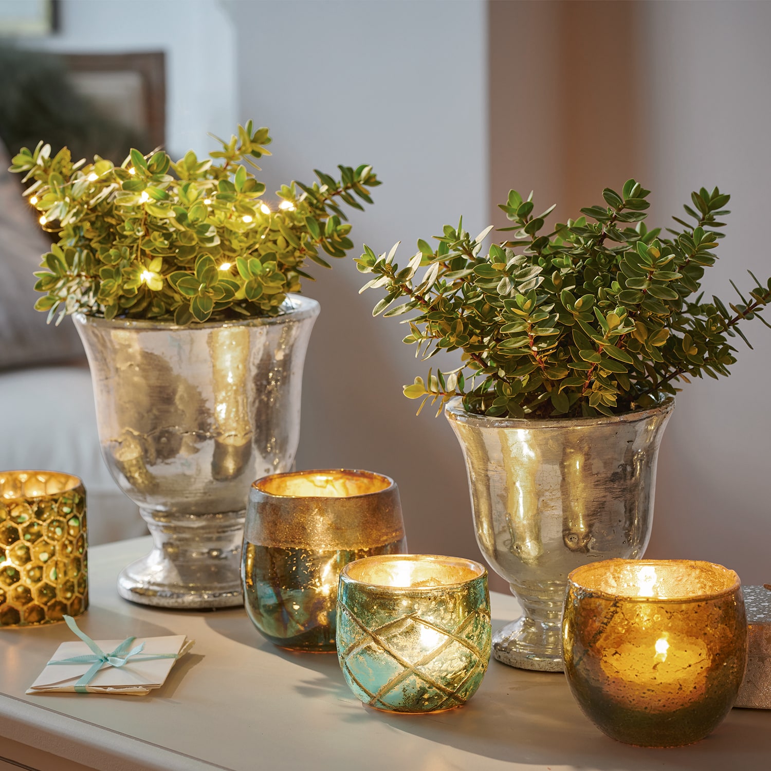 Pots argentés décoratifs avec plantes vertes et photophores en verre lumineux sur une table