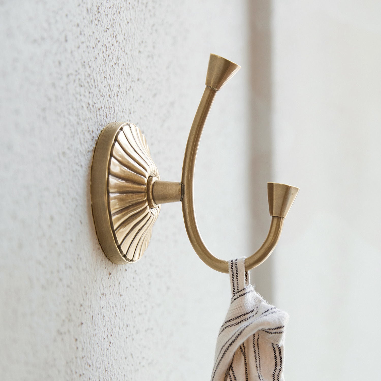 Haak Terling Dubbele messing wandhaak met decoratieve basis en opgehangen stof, vintage stijl