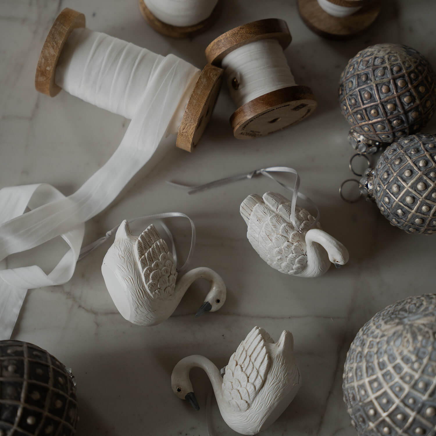 Décorations cygnes en céramique blanche avec ruban et bobines en bois avec ruban blanc sur table en marbre