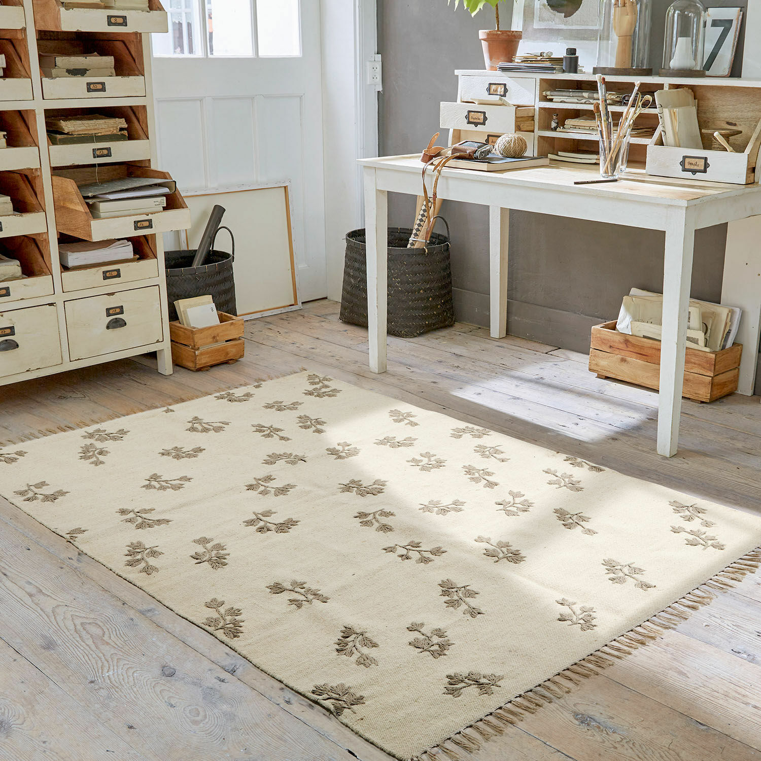 Vloerkleed Galorique Beige vloerkleed met bloemenpatroon en franjes op houten vloer in lichte werkkamer