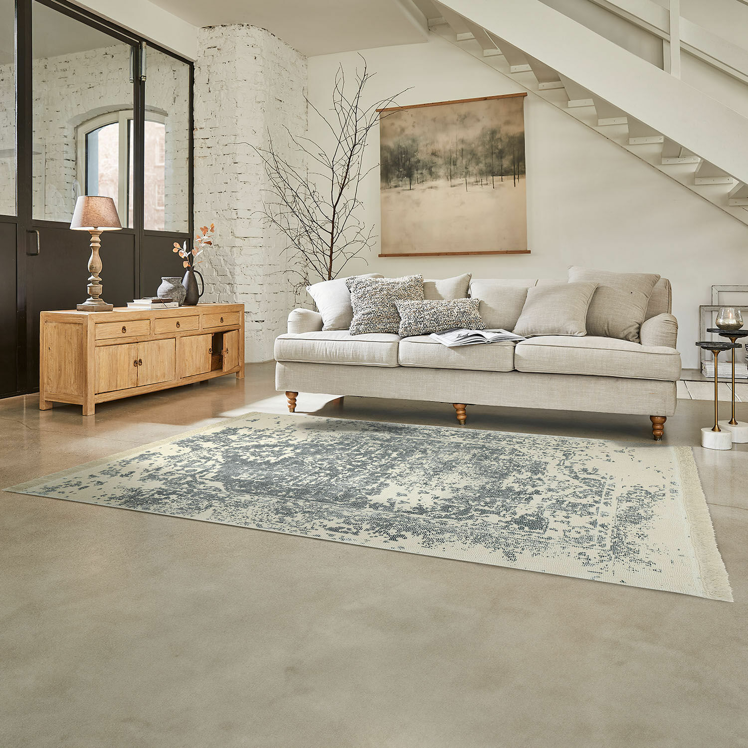Canapé beige avec coussins sur tapis gris dans un salon lumineux avec buffet en bois et décoration murale