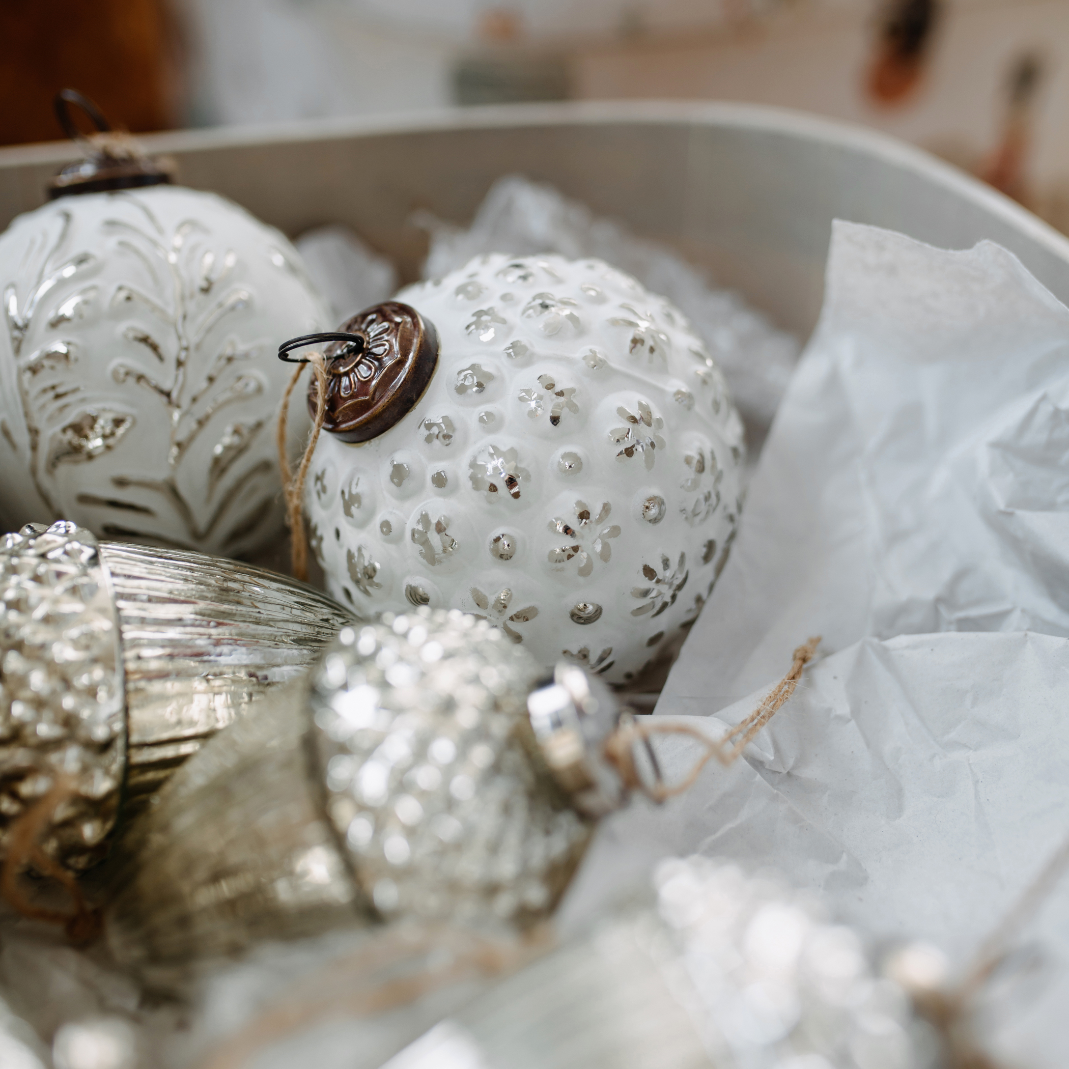 Boules de Noël blanches et argentées en verre et métal avec motifs, rangées dans une boîte avec du papier