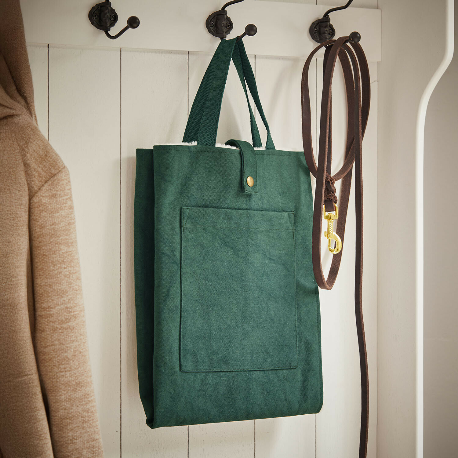Tapis pour animaux Felliro Sac vert en tissu suspendu sur un porte-manteau blanc à côté d'une laisse marron et d'un manteau beige