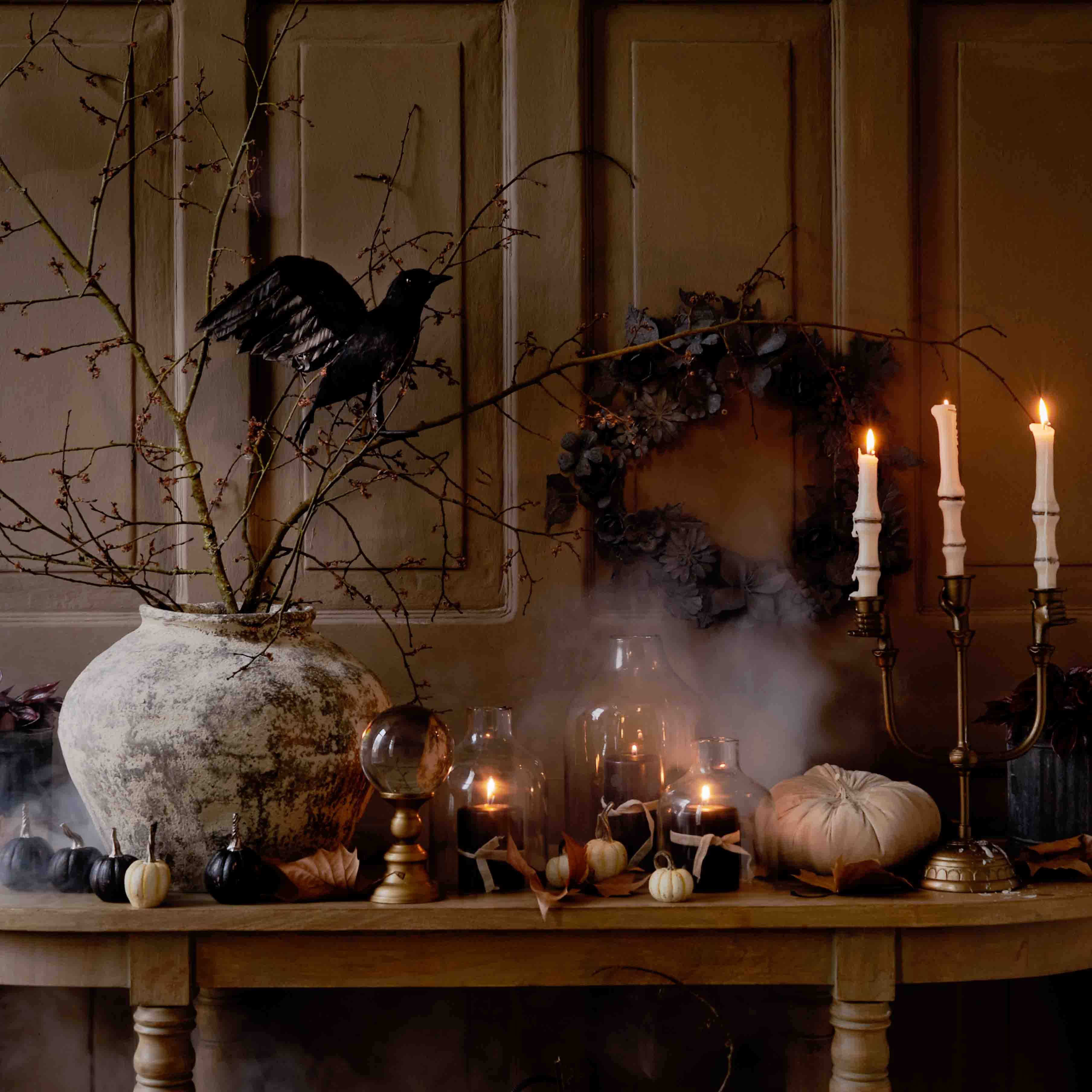 Table décorative d'automne avec grand vase en céramique, bougies allumées et oiseau noir sur branche
