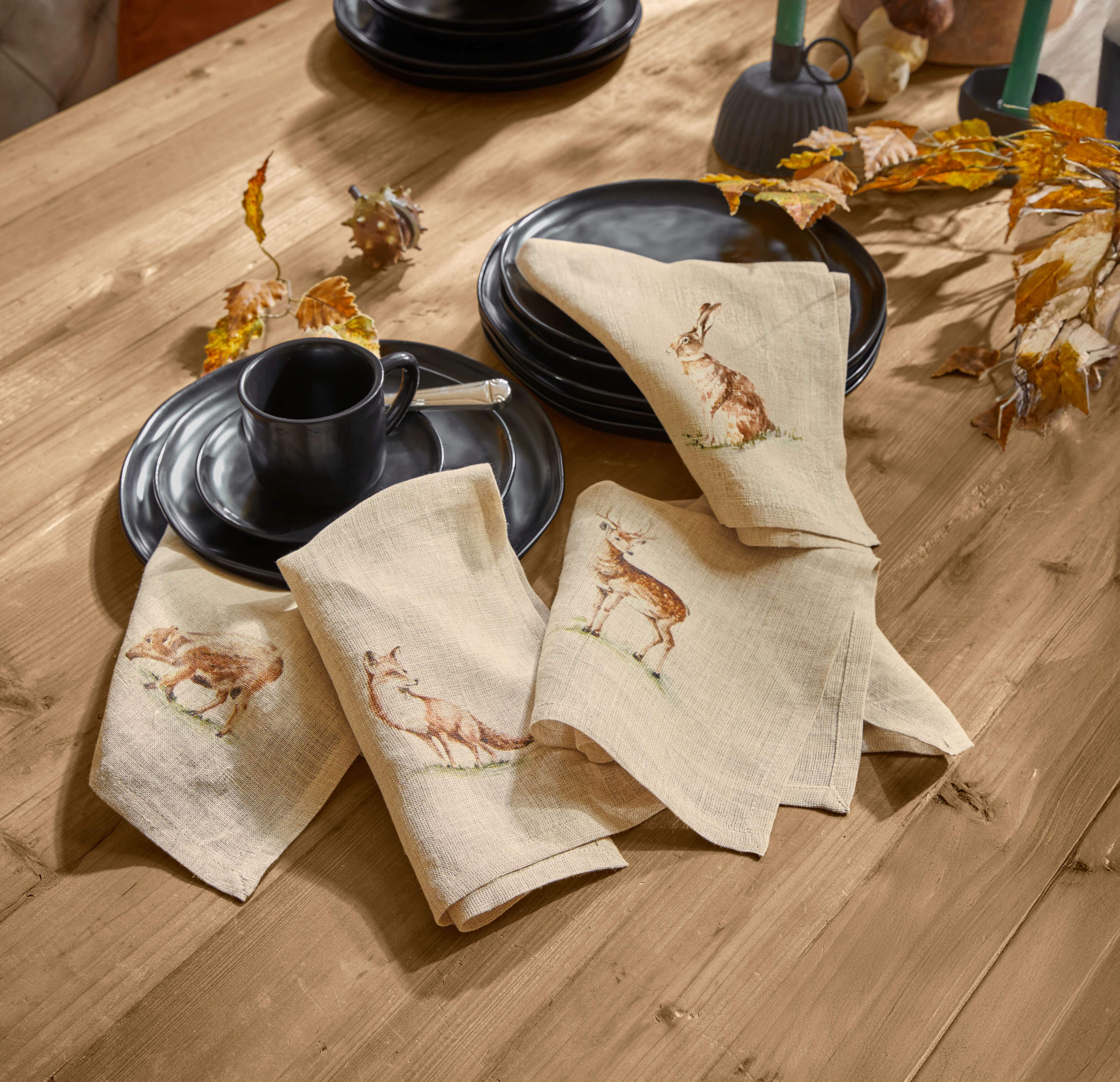 Beige linnen servetten met bosdierenprint op houten tafel met zwart servies