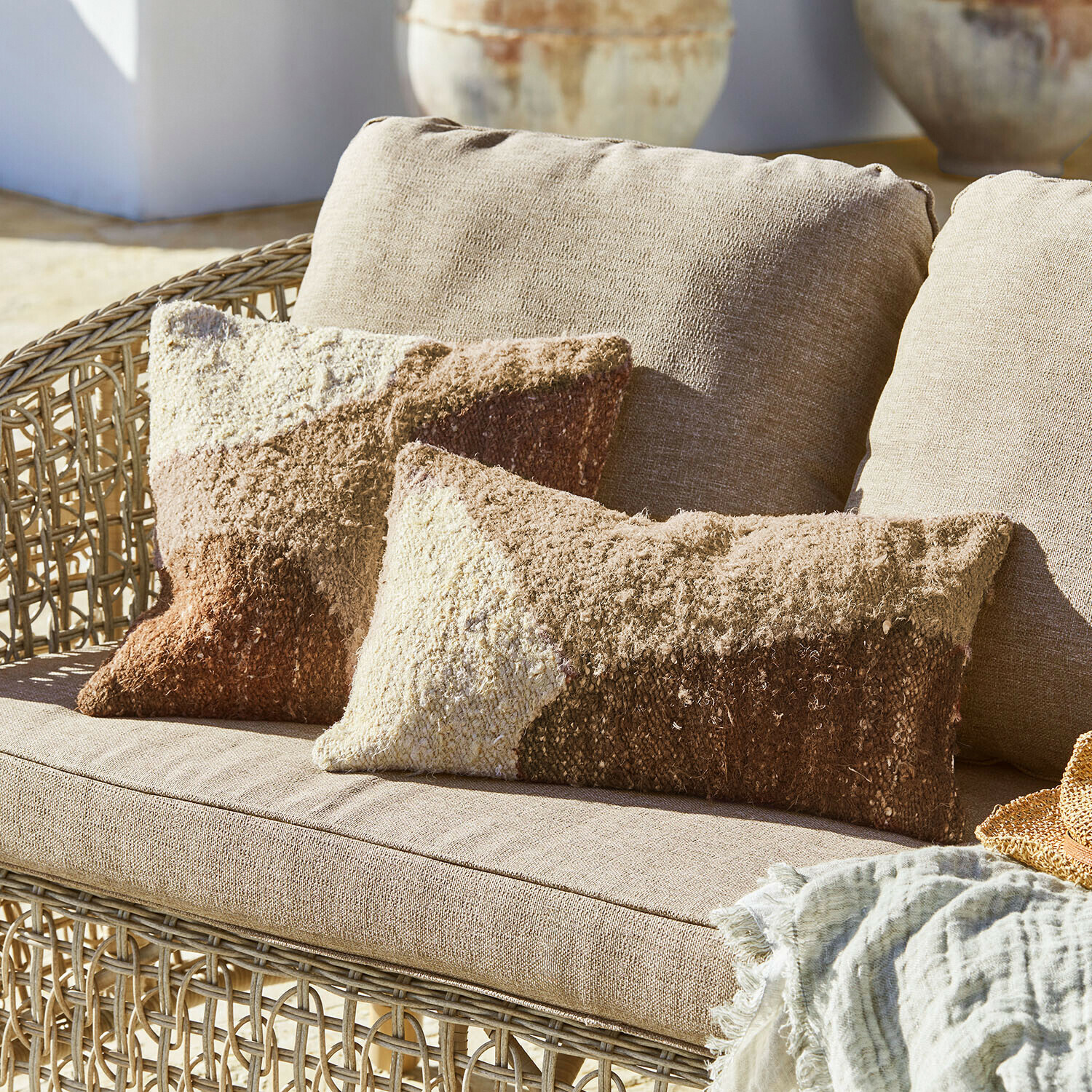 Beige rotanbank met zachte kussens in bruin- en crèmekleuren, decoratief textieldeken