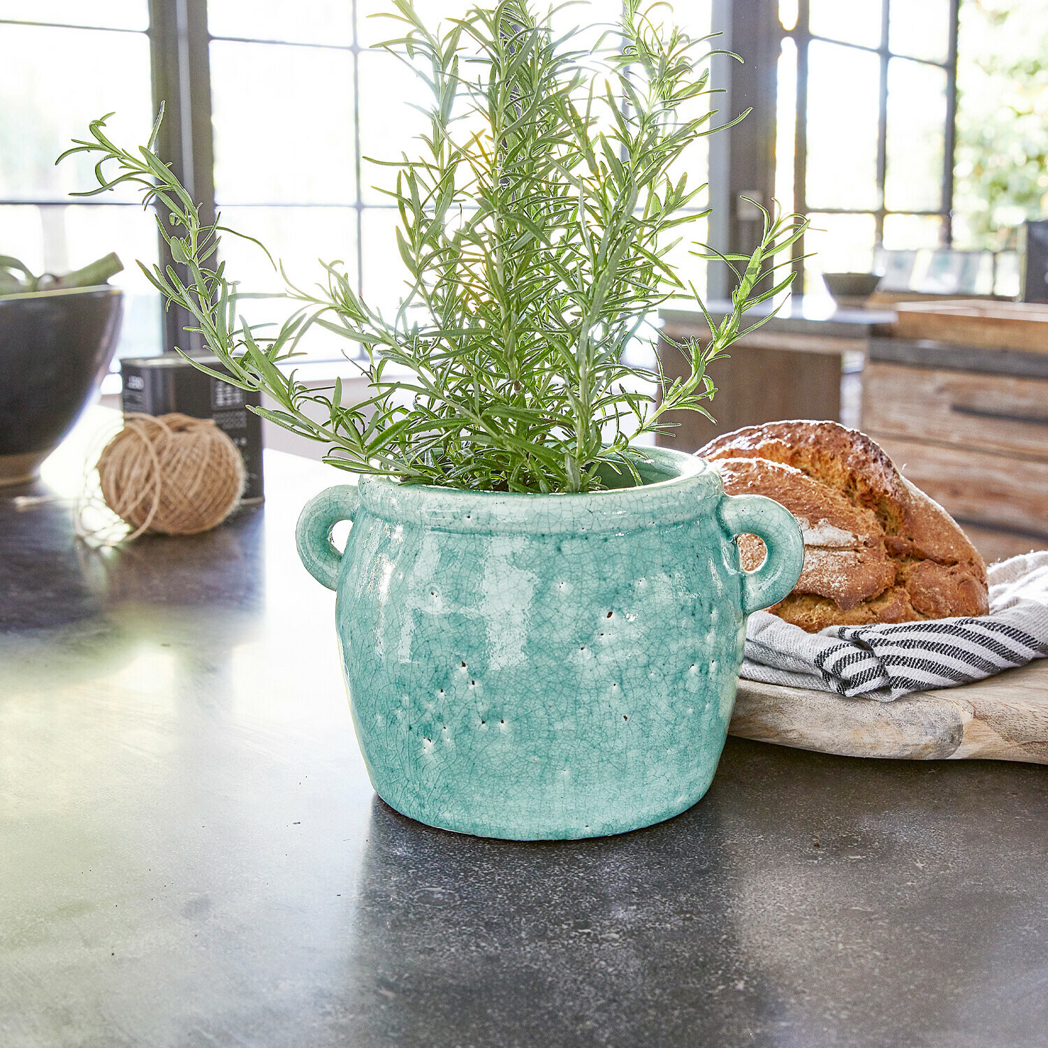 Turquoise keramische pot met handvatten en groene plant op keukenblad met brood