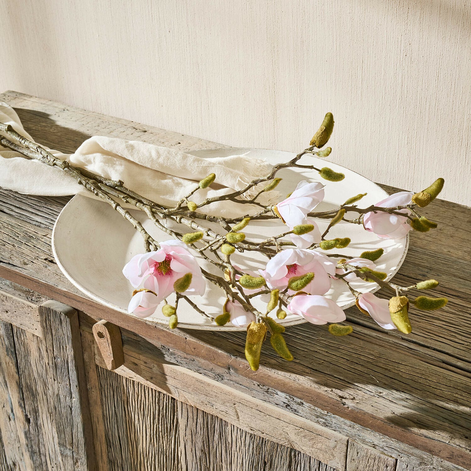 Decoratieve bloem set van 2 Aurélines Magnoliatakken met roze bloemen en groene knoppen op een wit bord op een rustieke houten tafel