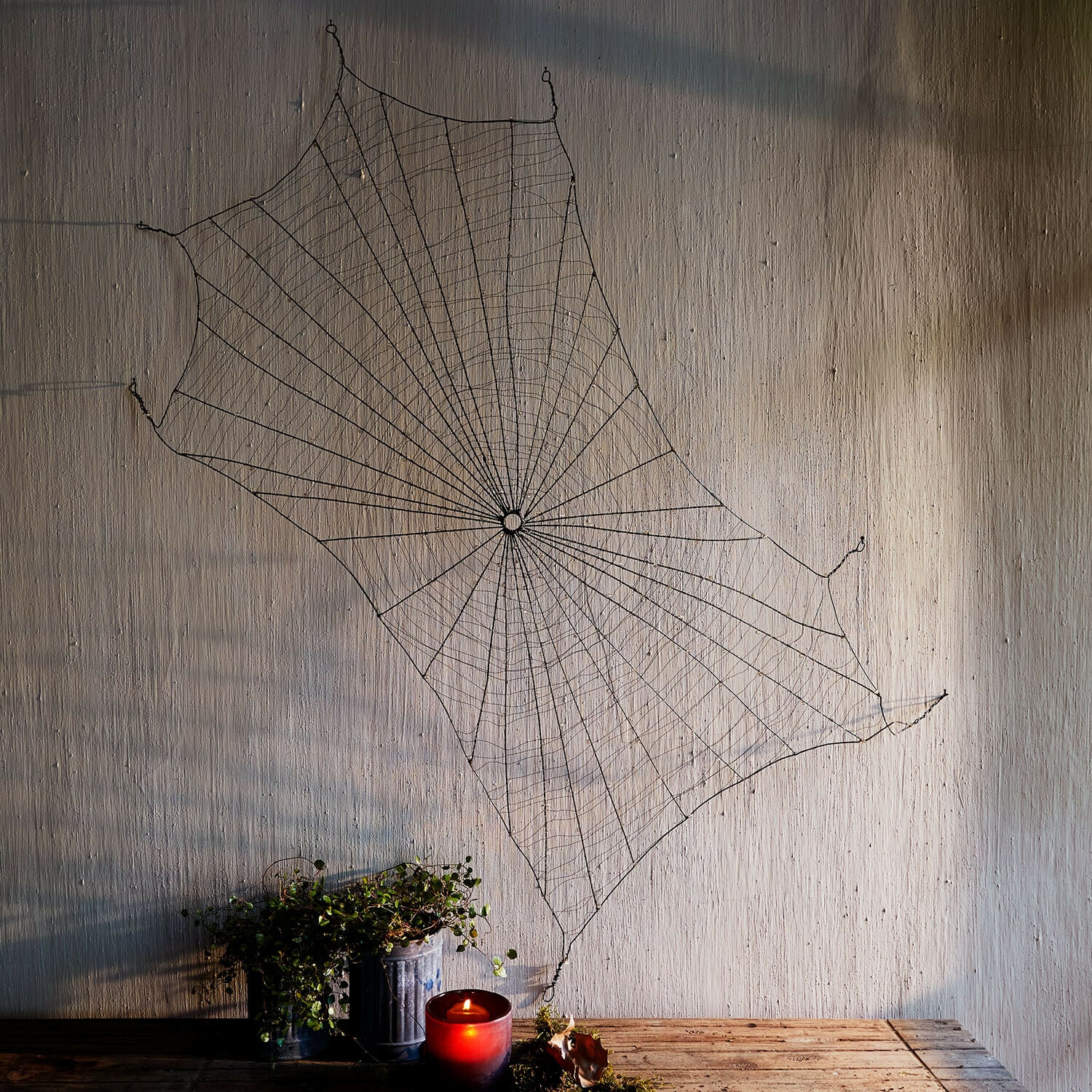 Decoratief spinnenweb Vexilnor Zwarte metalen spinnenweb wanddecoratie met rode kaars en plant op houten tafel