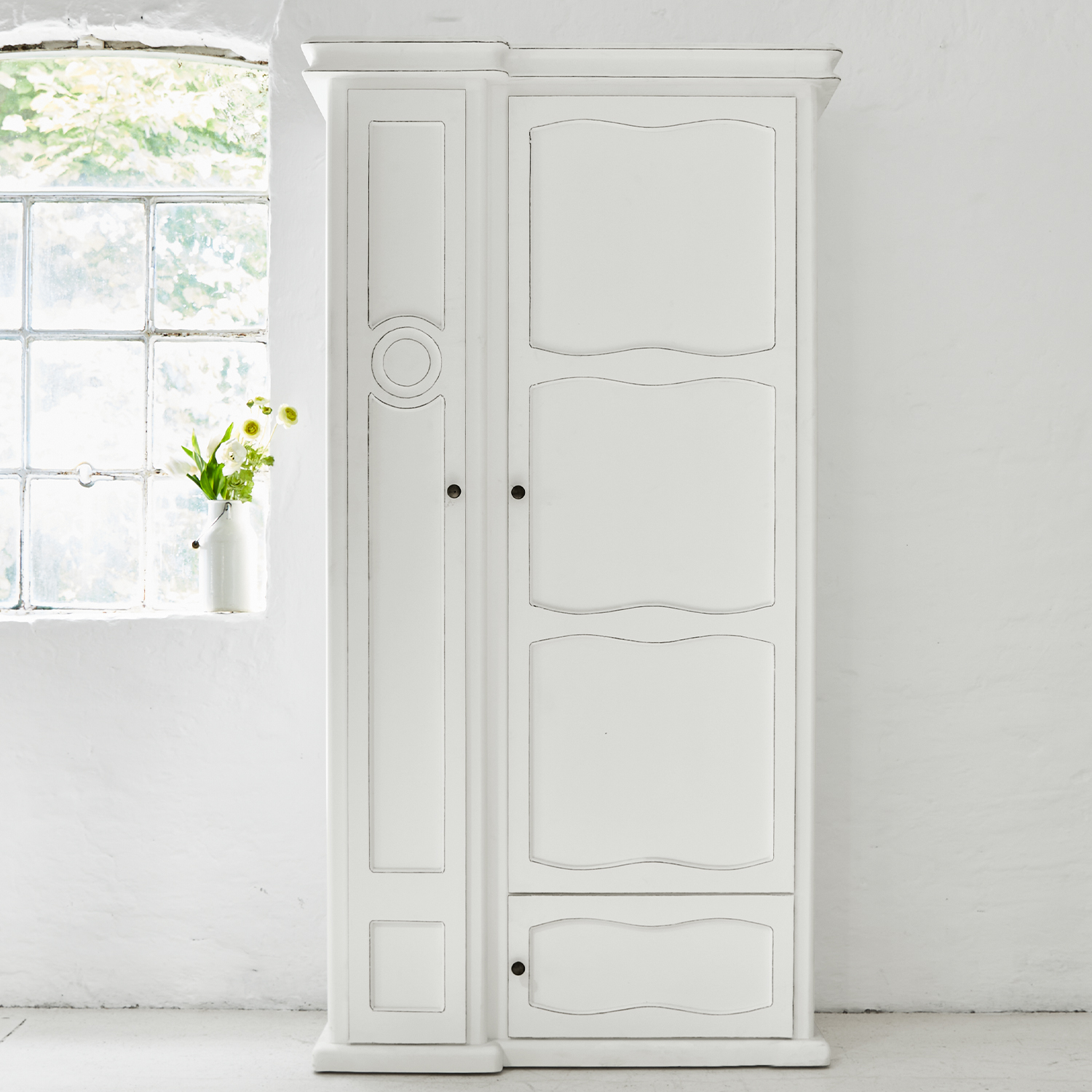 Witte houten kast met decoratieve panelen en metalen handgrepen in lichte kamer