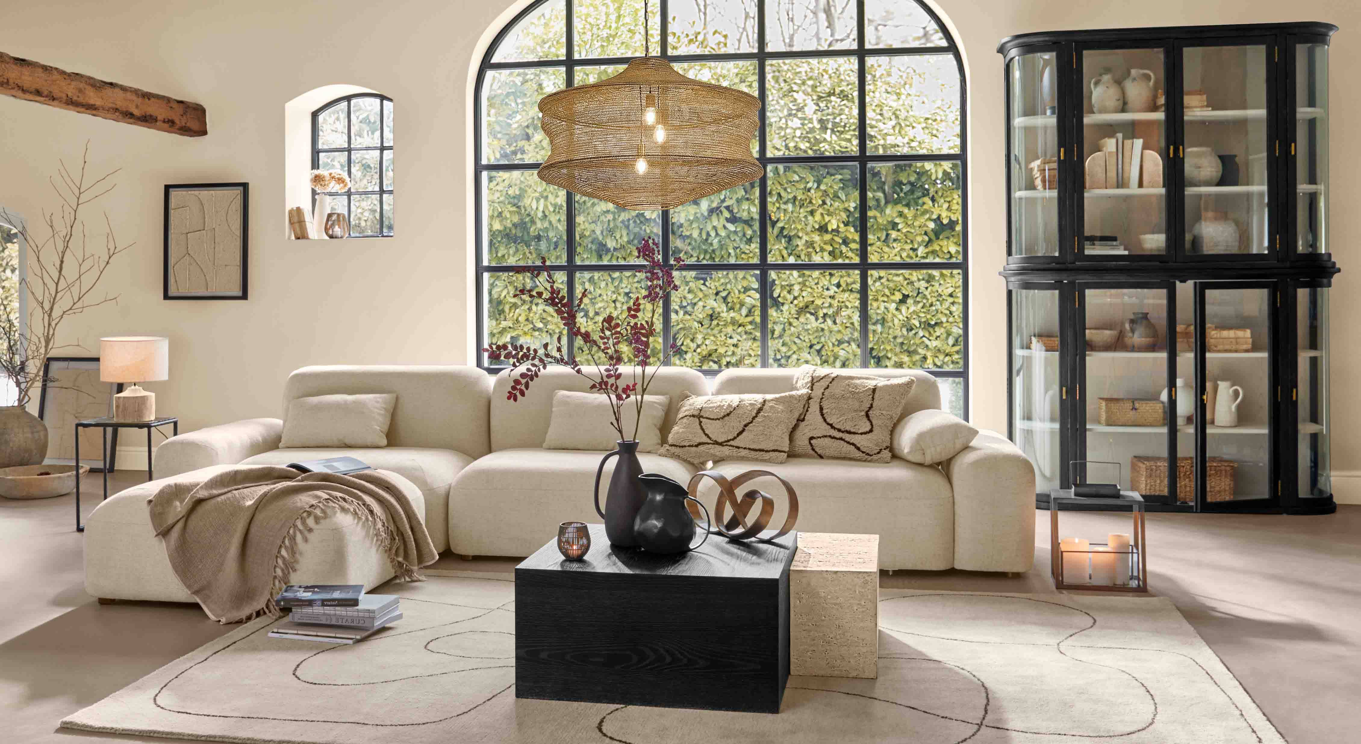 Gezellige woonkamer met beige bank, zwarte kast en groot raam, moderne verlichting en decoratie