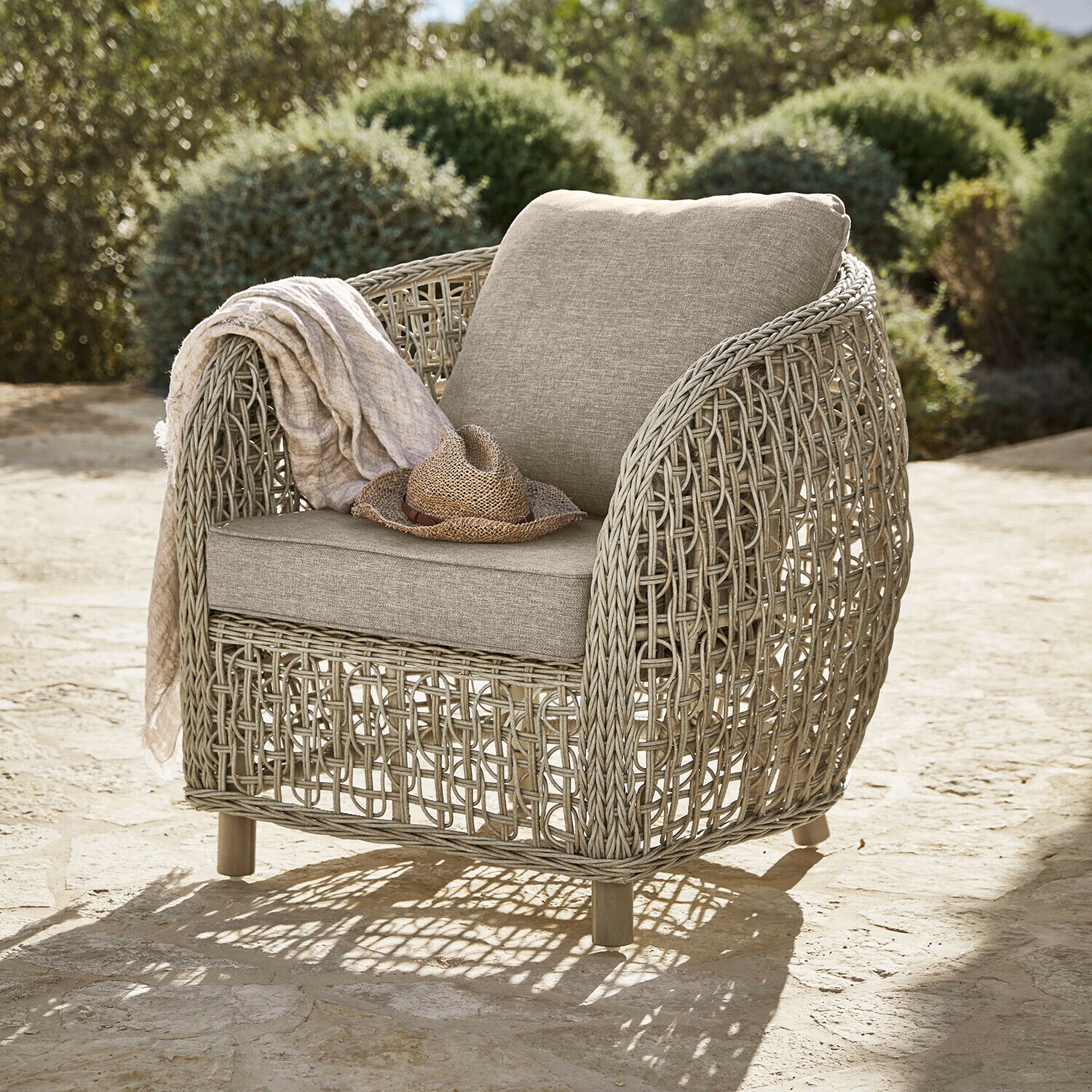 Fauteuil Ventiglio Fauteuil d'extérieur en rotin beige avec coussins beige clair, chapeau et plaid posés dessus