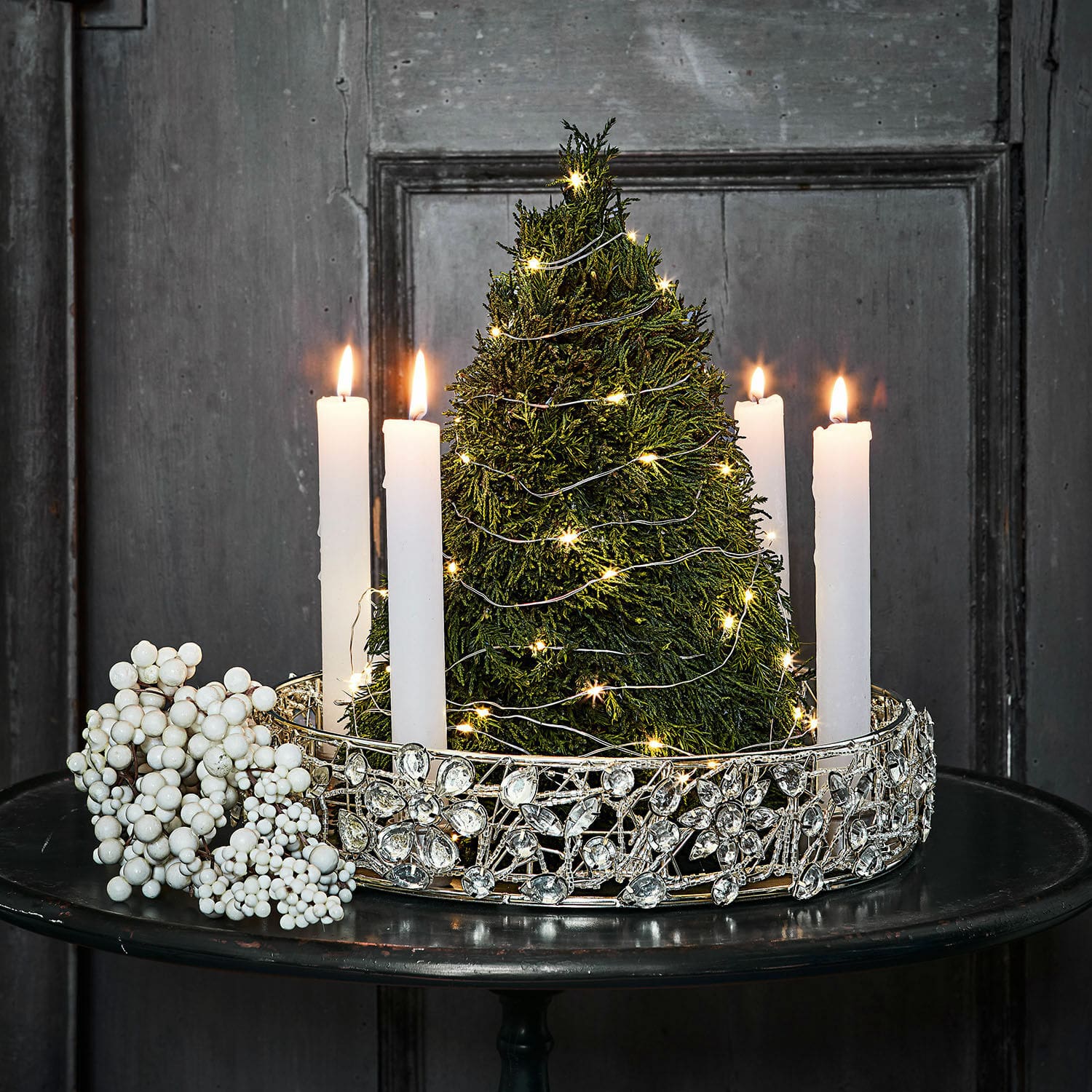 Bougeoir Hope Décoration de Noël avec sapin vert, bougies blanches et couronne argentée ornée sur une table noire