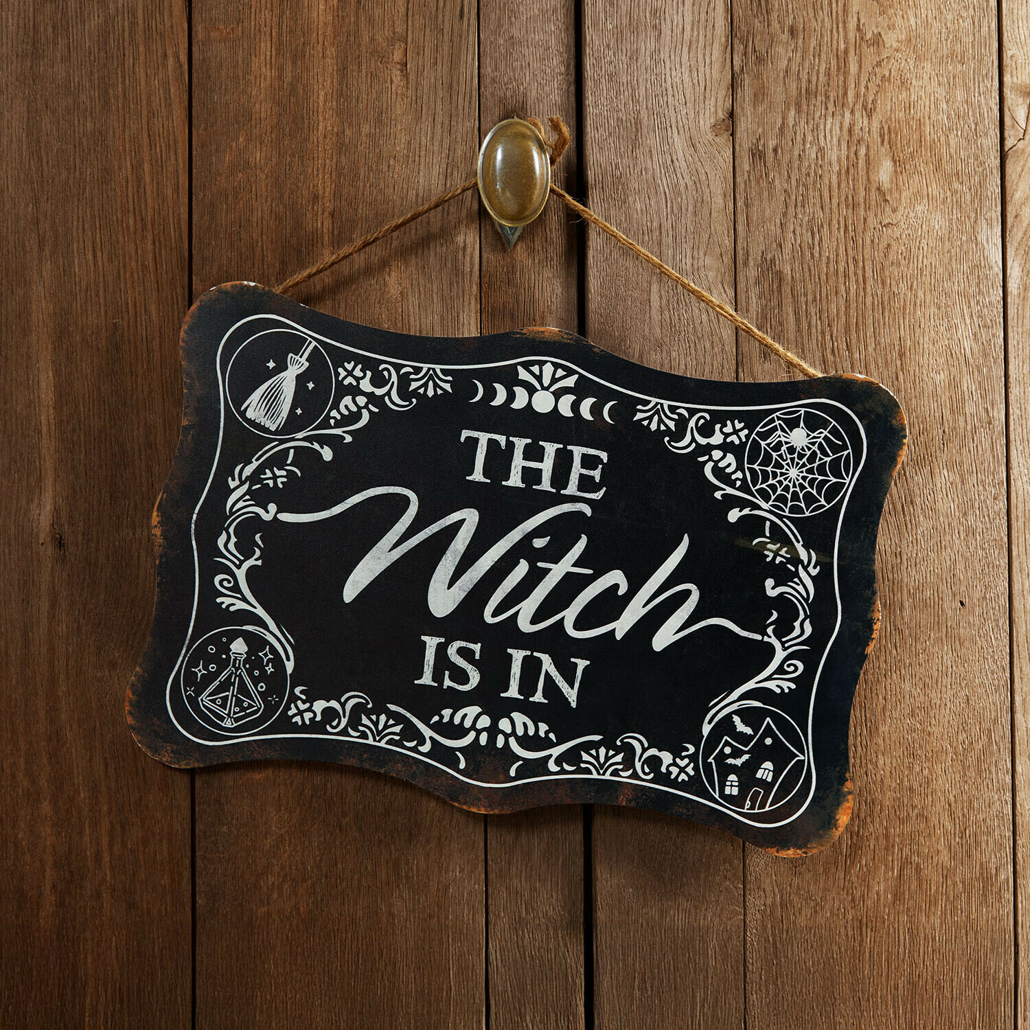 Decoratief bord Talmora Zwart houten bord met tekst The Witch is in en witte versieringen tegen houten achtergrond