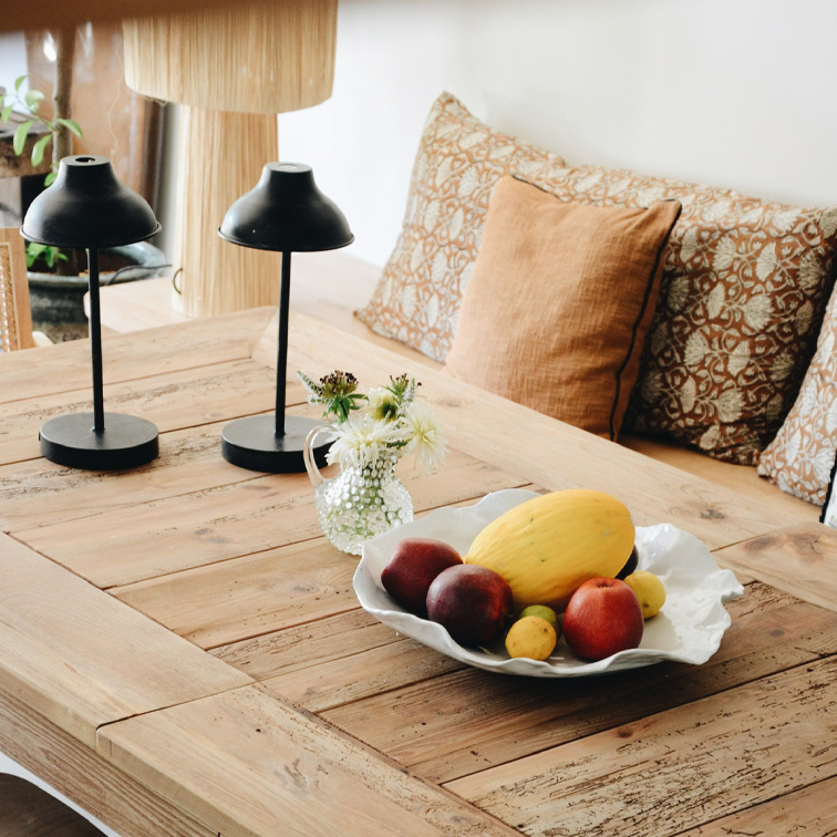 Table en bois avec bol blanc décoratif rempli de fruits et deux lampes noires dans un intérieur chaleureux