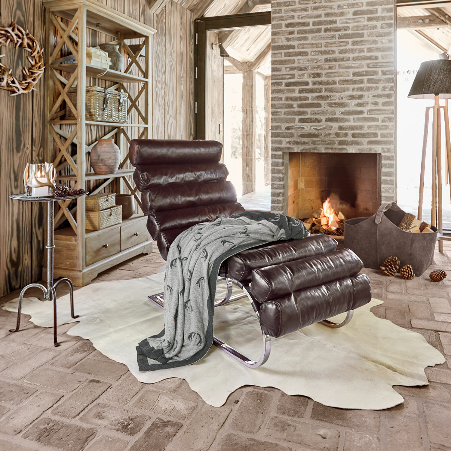 Tapis en peau de vache Edward Fauteuil en cuir marron avec base métallique sur tapis clair près d'une cheminée dans un intérieur rustique