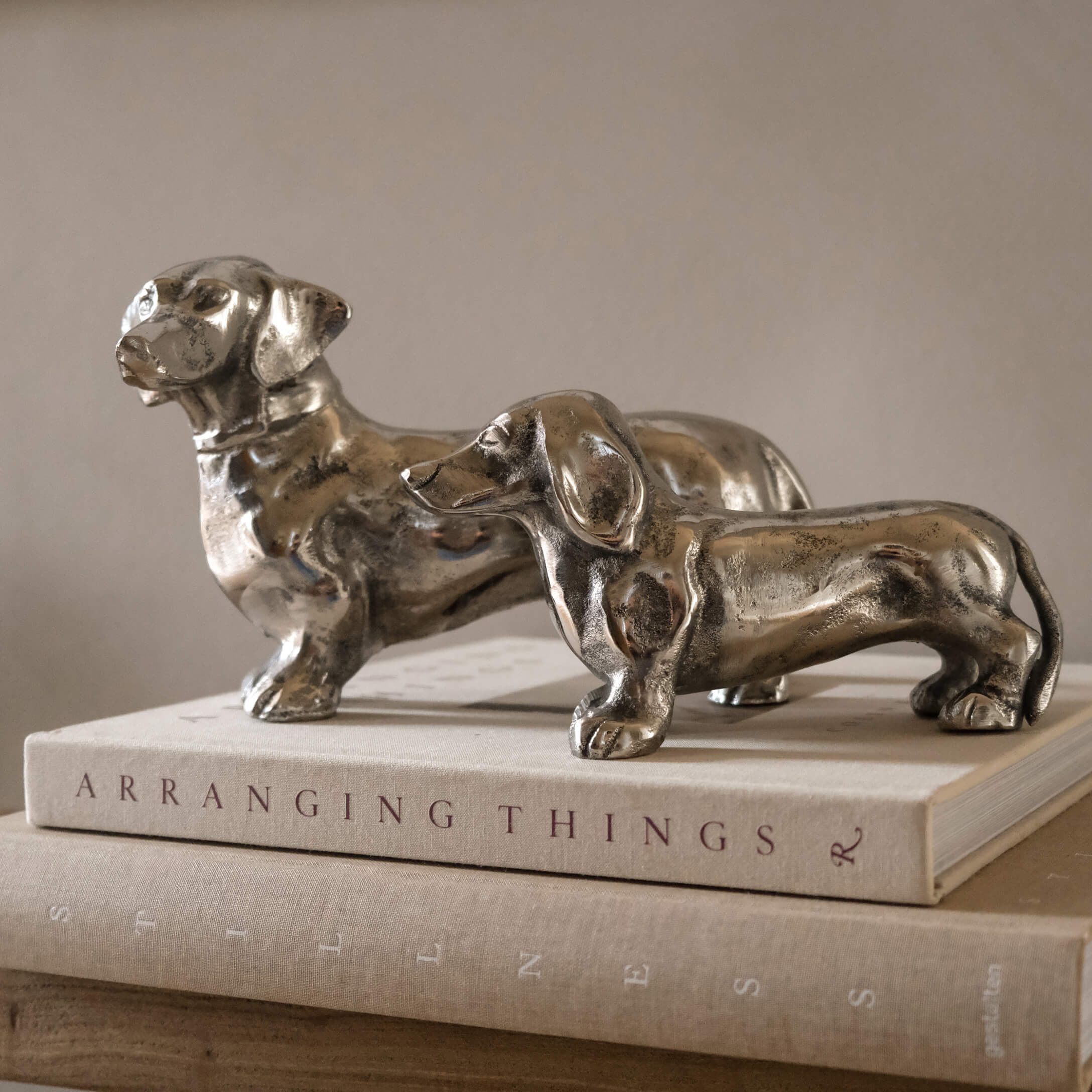 Deux figurines de teckels en métal argenté posées sur des livres pour décoration intérieure