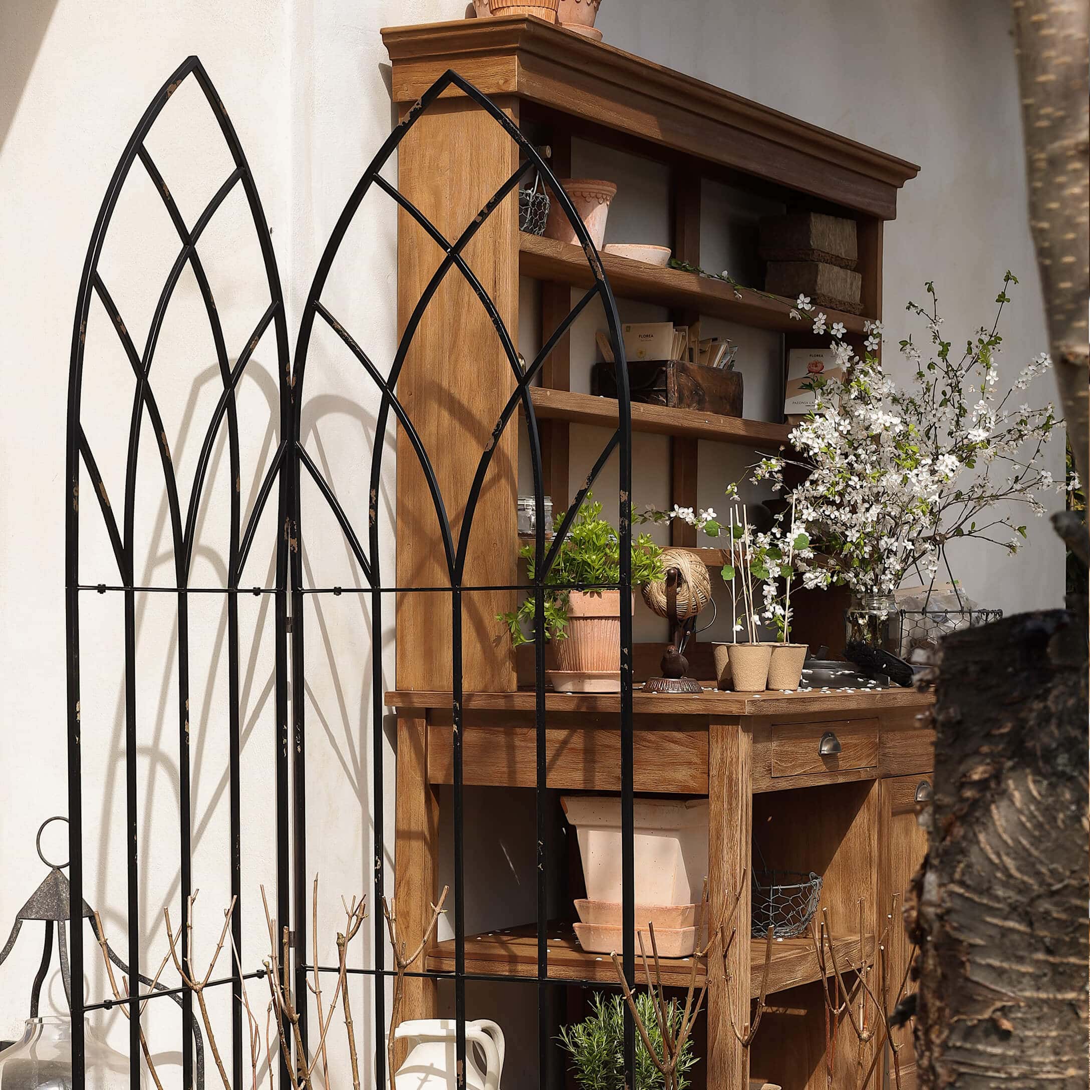 Grille de jardin en métal noir avec motif en arc devant une étagère en bois avec pots et fleurs
