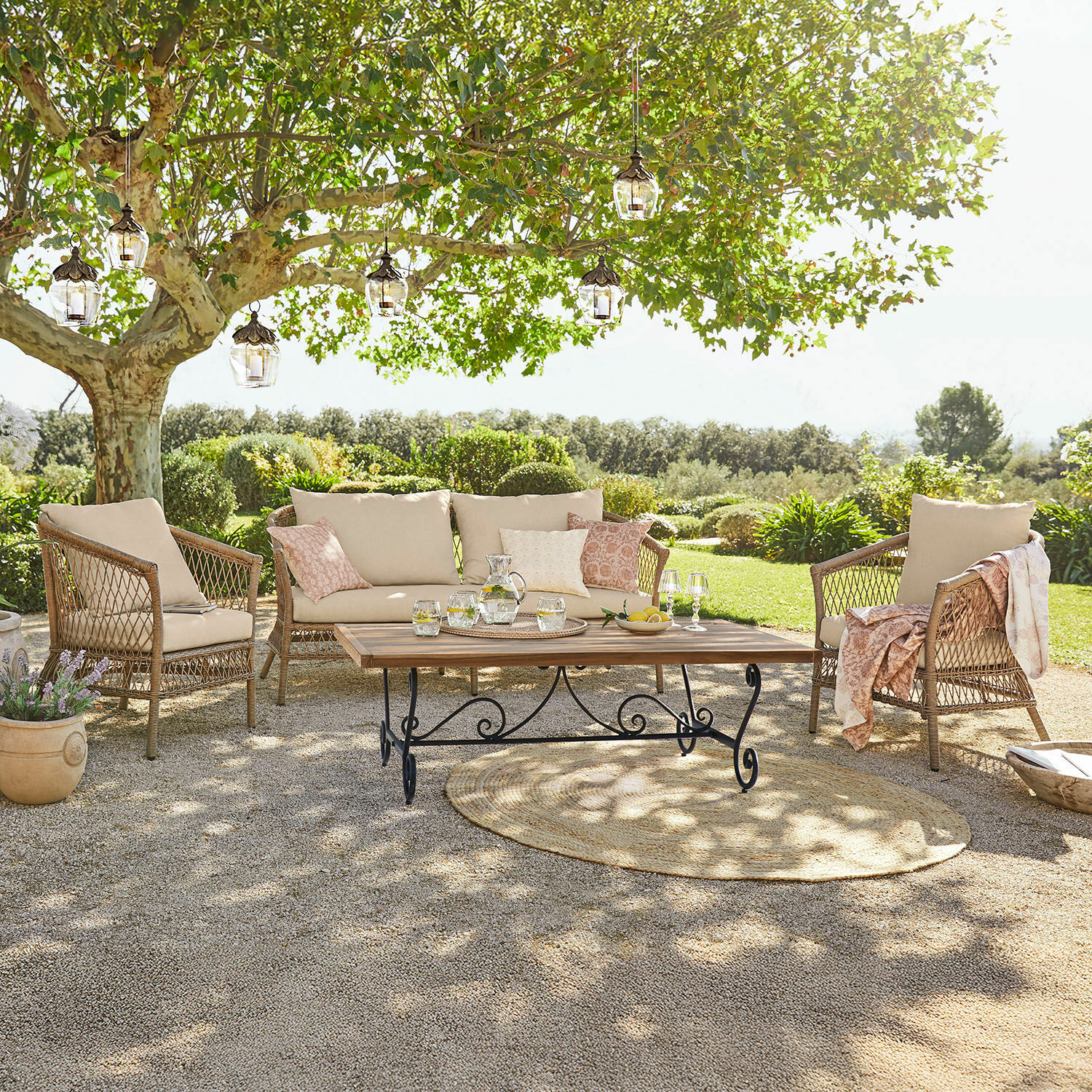Zithoek Farington Tuinmeubelset van rattan met beige kussens en houten tafel op terras in groene tuin