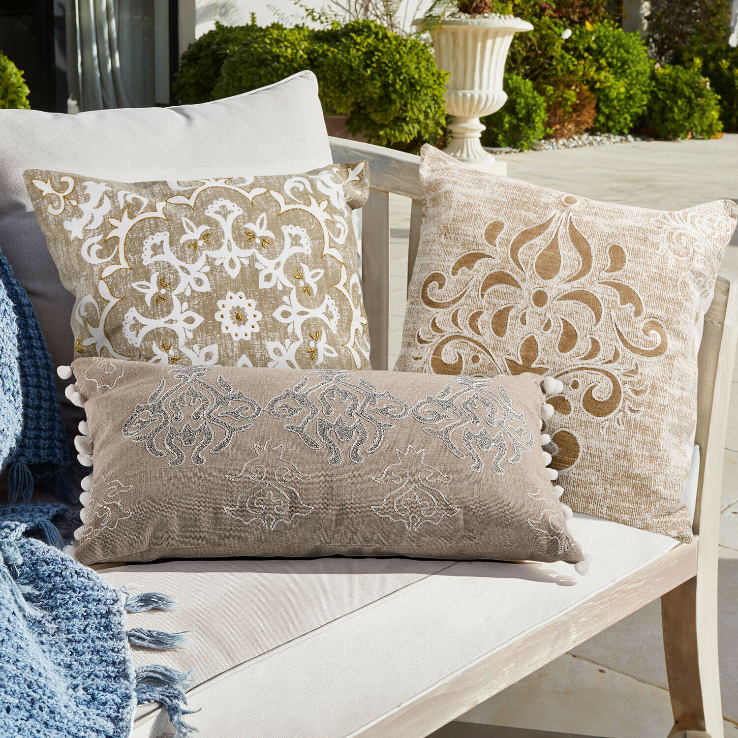 Lot de 3 housses de coussins Emelin Ensemble de coussins décoratifs beige et blanc avec motifs sur un canapé clair en terrasse