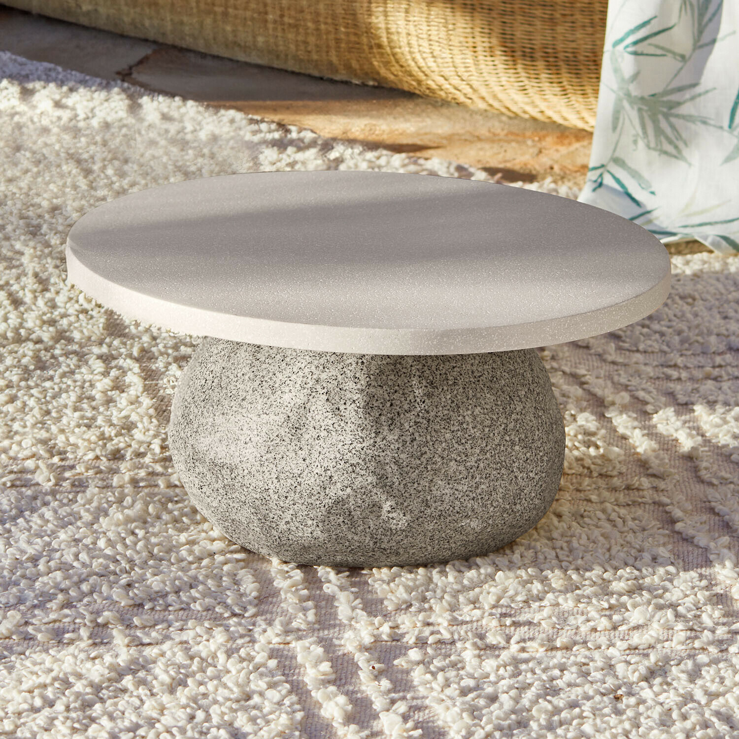 Table basse Orivana Table basse ronde en pierre grise posée sur un tapis clair, design moderne et épuré