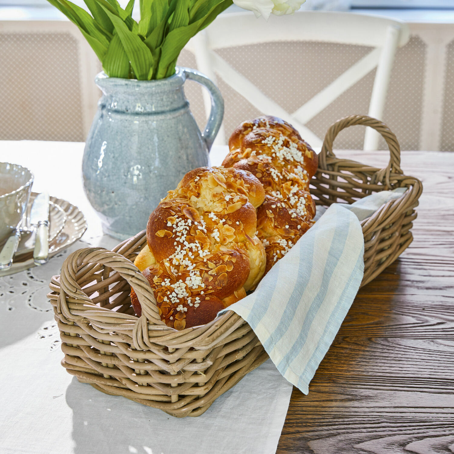 Corbeille Balmis Panier en osier avec poignées contenant du pain brioché et un torchon en lin sur une table en bois