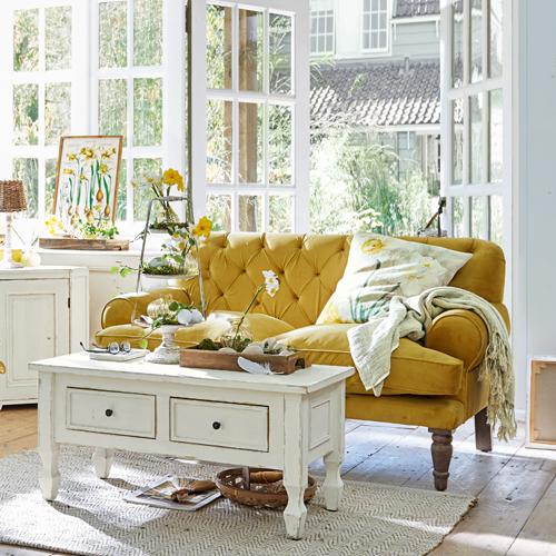 Geel fluwelen vintage bank in lichte woonkamer met witte houten salontafel en decoraties