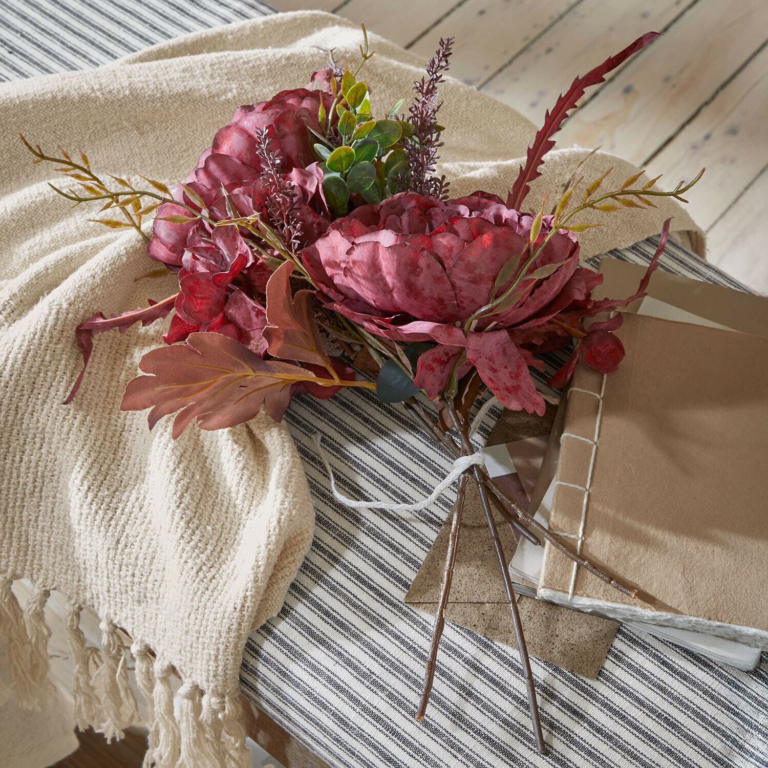 Sierboeket Rivière Ambrée Boeket van kunstmatige rode bloemen met groen blad op een beige plaid en gestreept tafelkleed