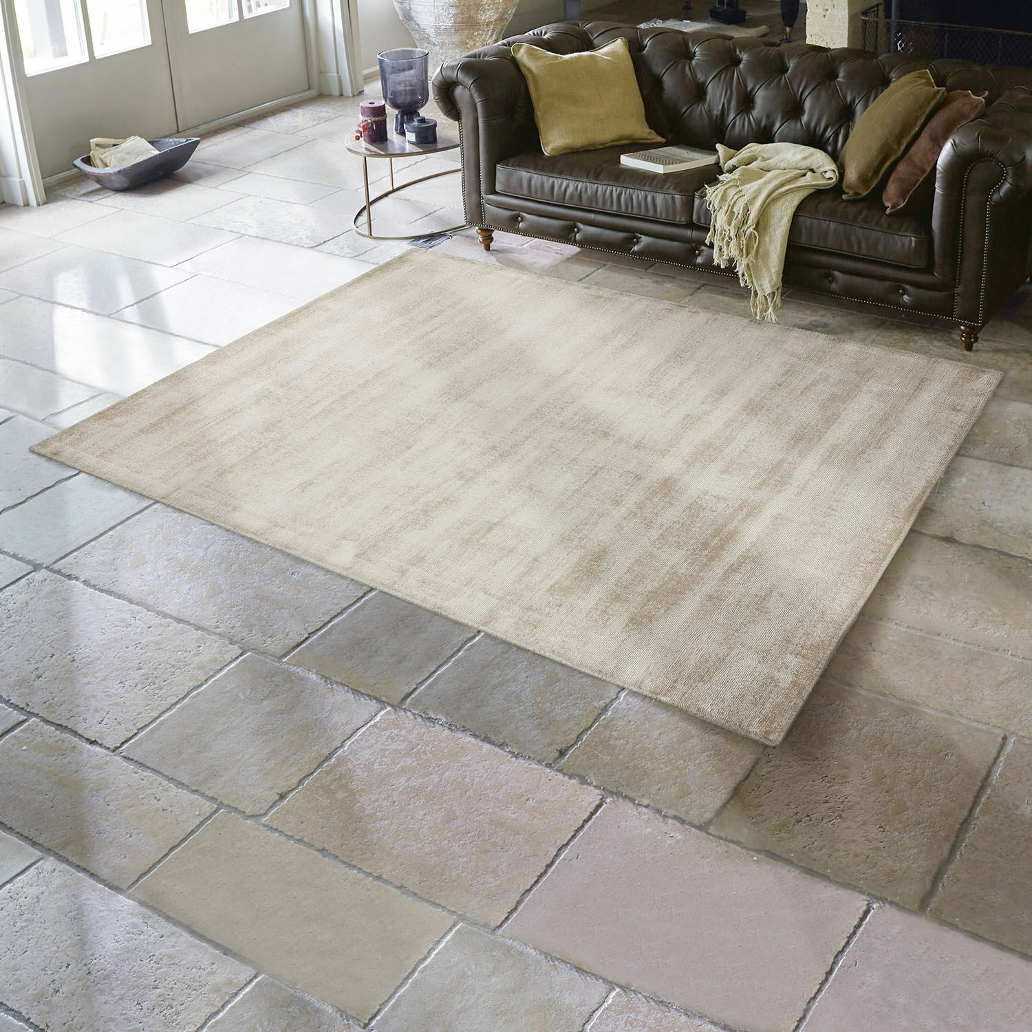 Tapis Mariselle Tapis beige en tissu doux sur sol en pierre dans un salon avec canapé en cuir marron