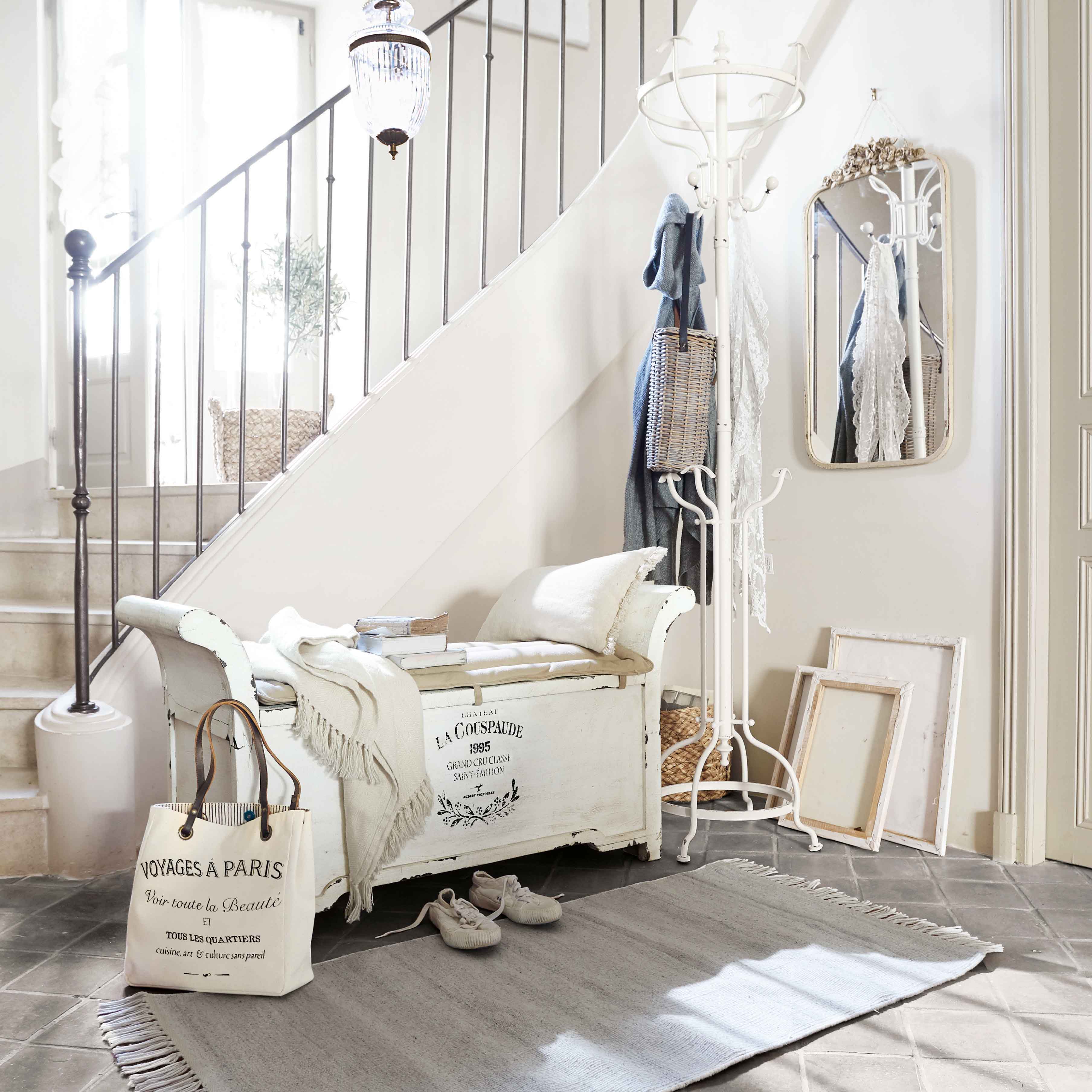 Banc en bois blanc avec coussin et plaid dans un hall lumineux avec porte-manteau et miroir