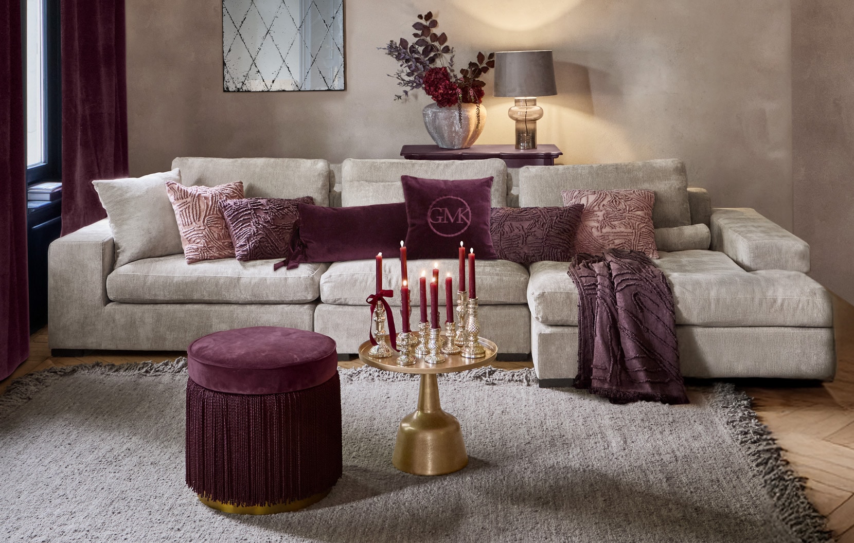 Beige bank met paarse kussens en bordeaux poef in stijlvolle woonkamer met decoratieve kaarsen