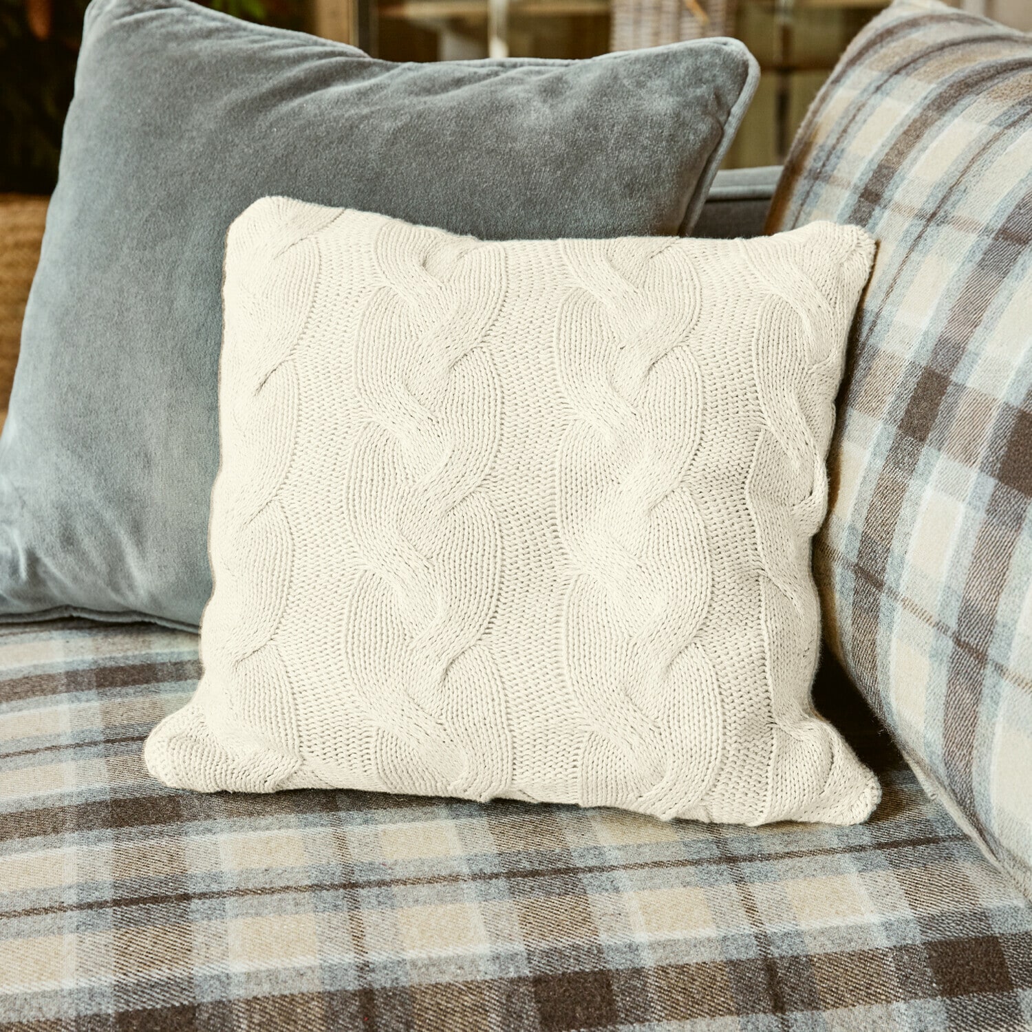 Kussenhoes Arnhem Beige gebreid kussen met vlechtpatroon op geruite bank, sfeervolle woondecoratie