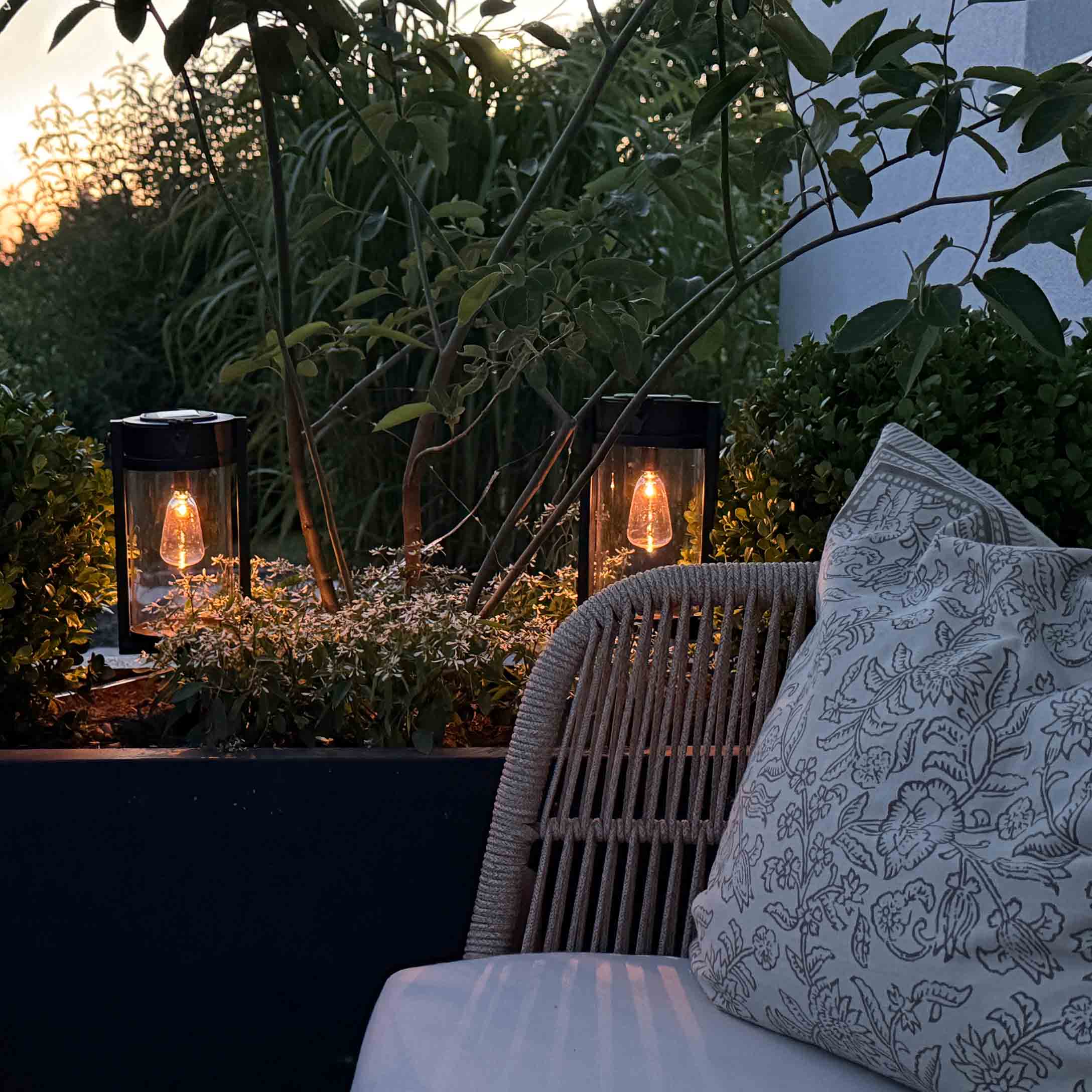 Lampes de jardin en métal noir avec lumière chaude parmi les plantes vertes sur la terrasse