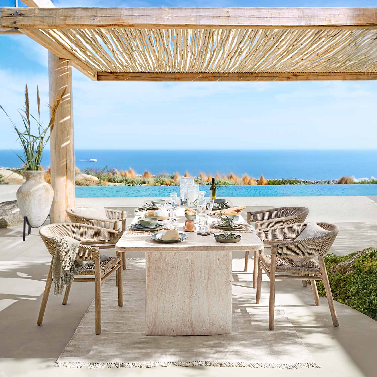 Salle à manger extérieure avec table en pierre naturelle et chaises en osier face à la mer