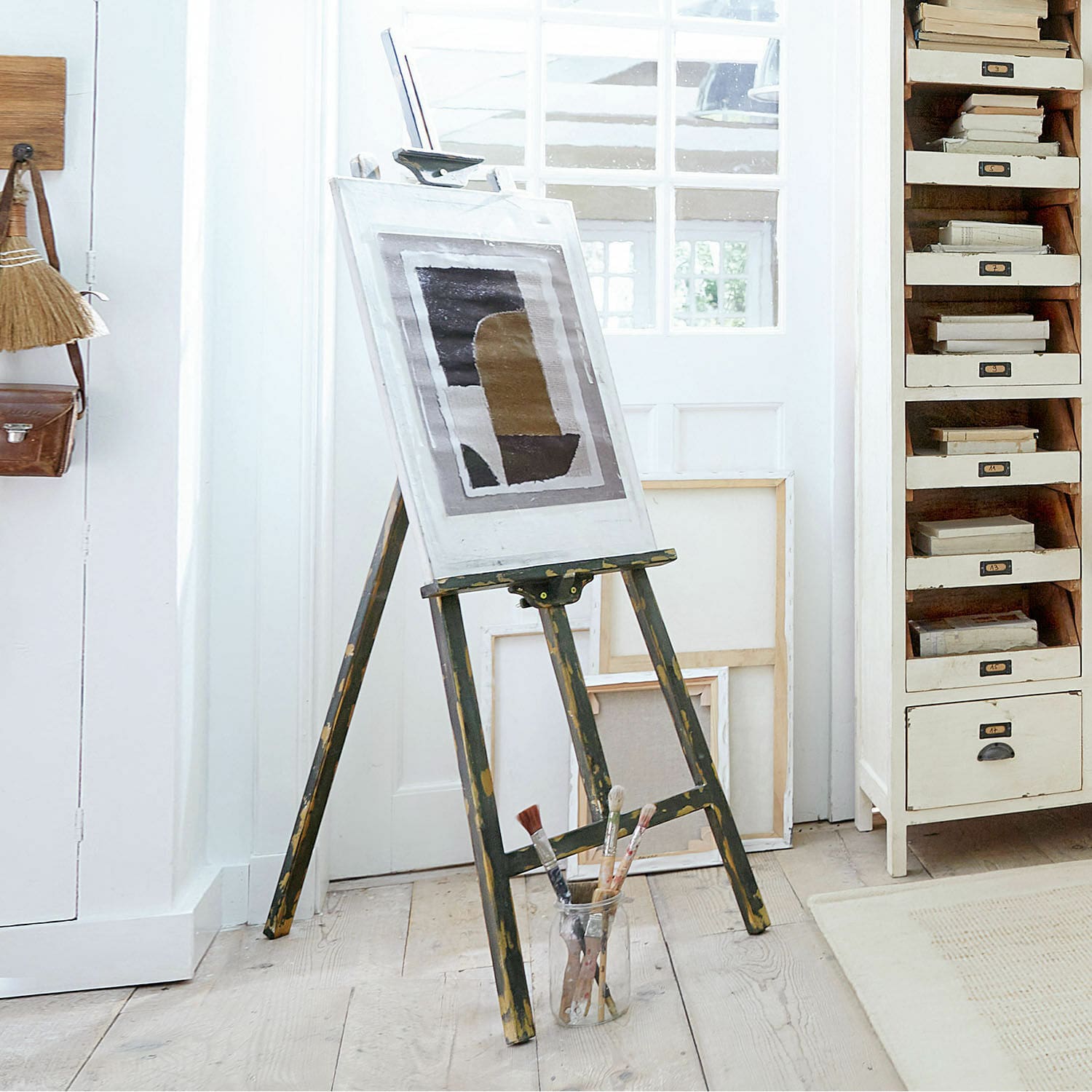 Chevalet Arabella Chevalet en bois vintage avec tableau et pinceaux sur sol clair dans un atelier lumineux