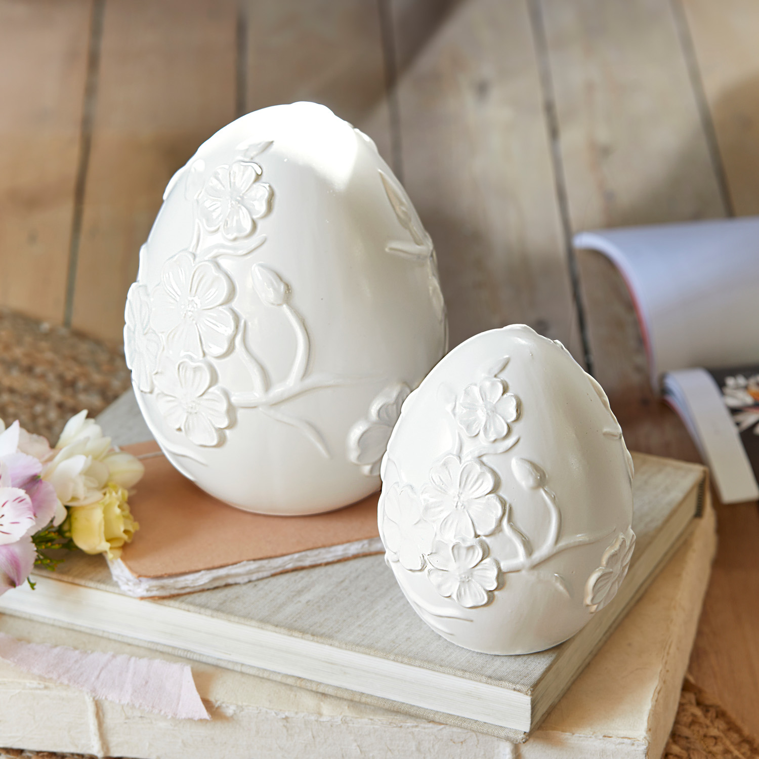 Œufs décoratifs en céramique blanche avec relief floral posés sur des livres, décoration printanière