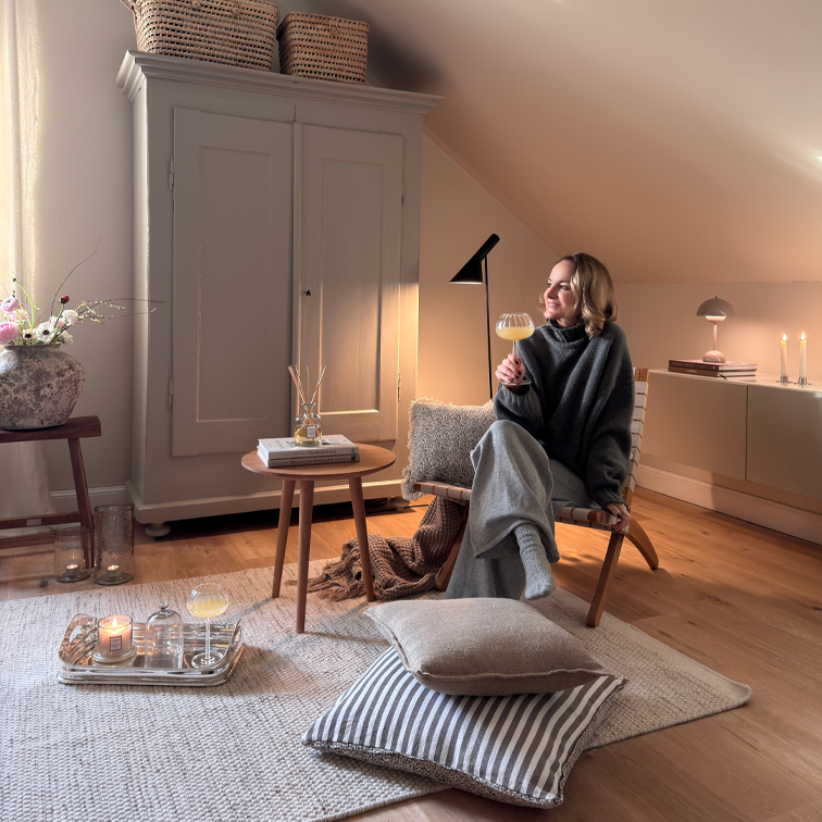 Coin détente chaleureux avec fauteuil en bois, plaid gris et bougies sur tapis clair