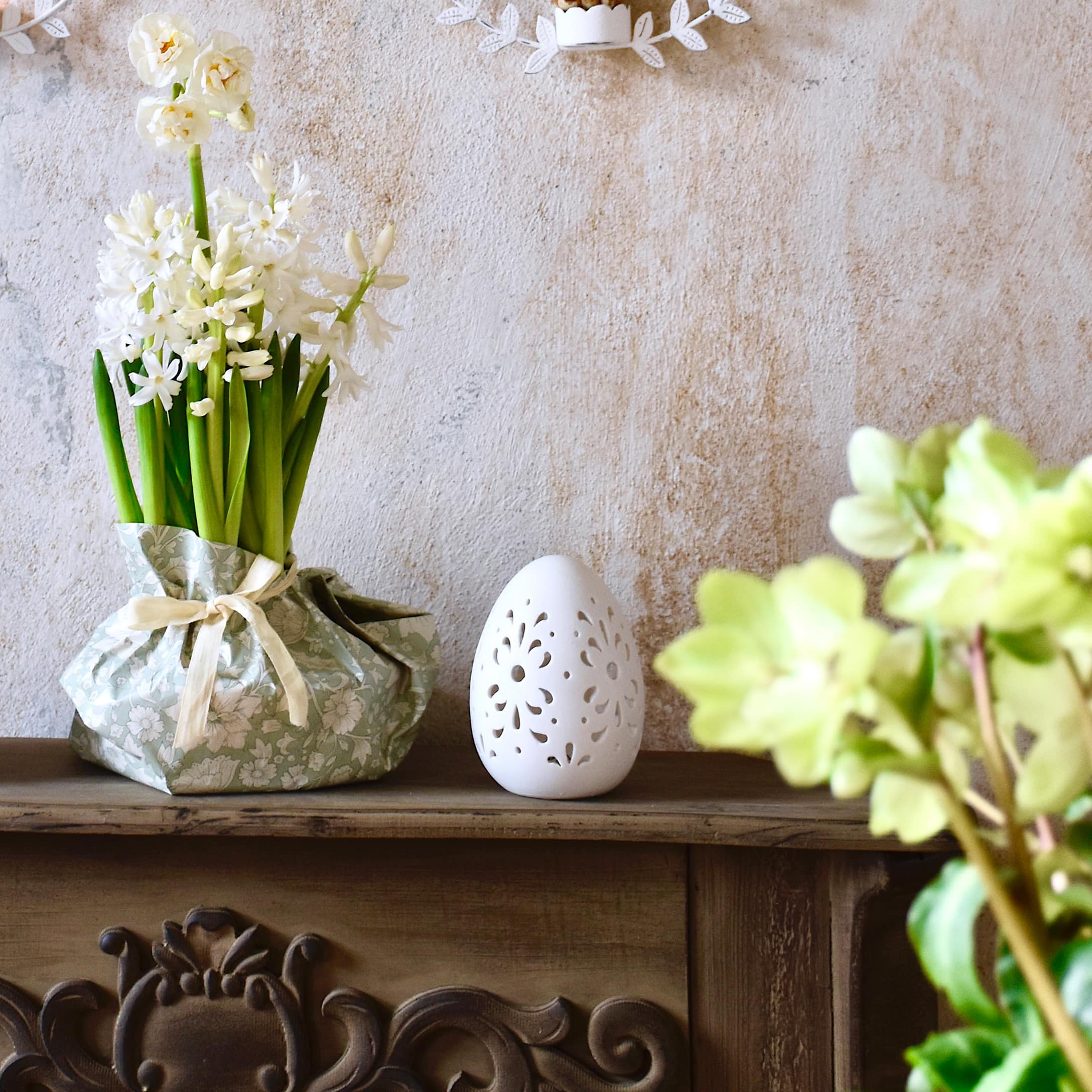 Fleurs blanches dans un emballage vert décoratif et œuf en céramique blanche sur une étagère en bois