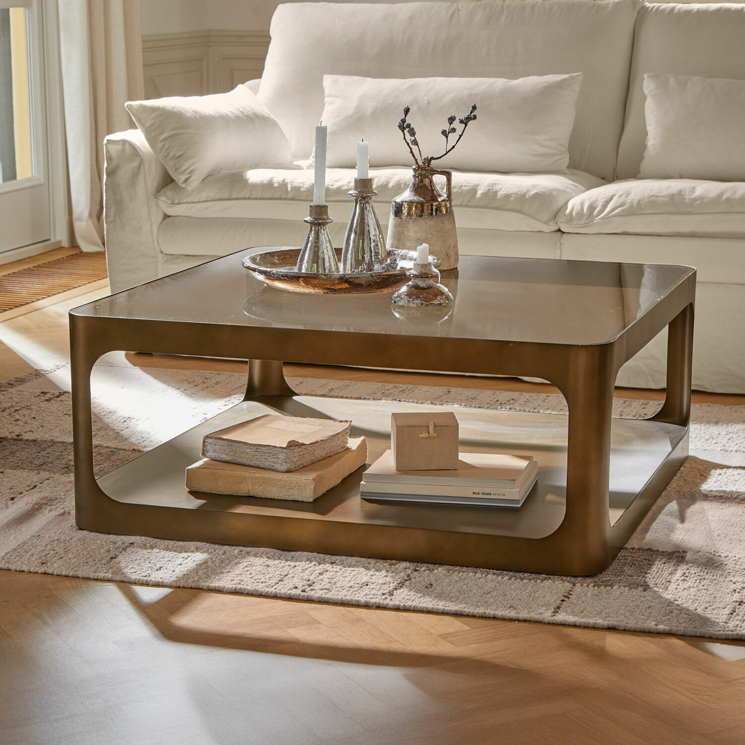 Table basse carrée en métal couleur laiton avec étagère et décoration sur tapis clair