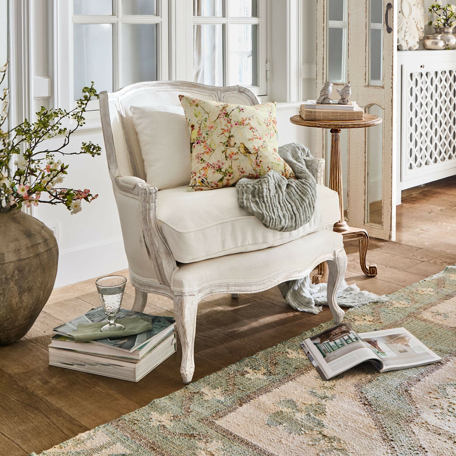 Fauteuil Kingswinford Fauteuil en bois blanc avec coussin fleuri et plaid gris dans un salon lumineux et chaleureux