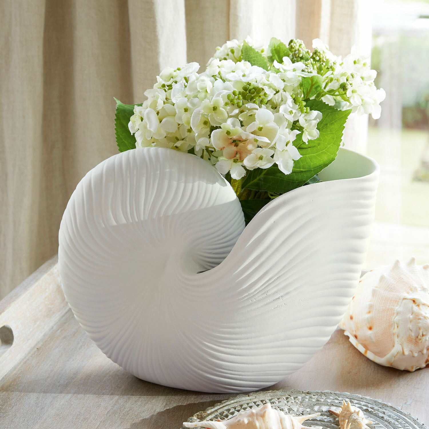 Bloempot Manteur Witte keramische bloempot in schelpvorm met witte bloemen en groene bladeren als decoratie